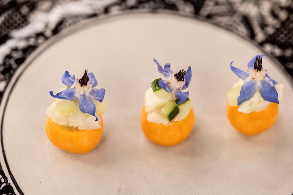 Three kumquat canapés topped with diced fruit and blue borage flowers