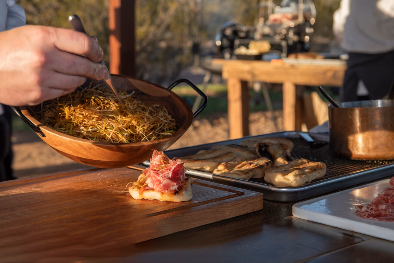 Chef tossing crispy fried herbs over a prosciutto flatbread outdoors