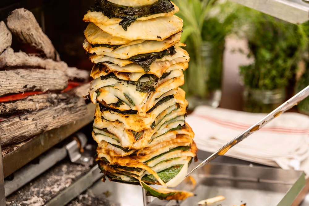 Skewer of stacked grilled onion and zucchini slices being basted over a fire