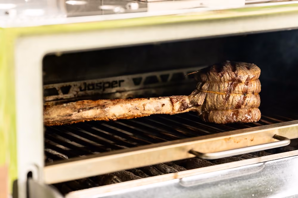 Tomahawk steak grilling inside a wood-fired smoker