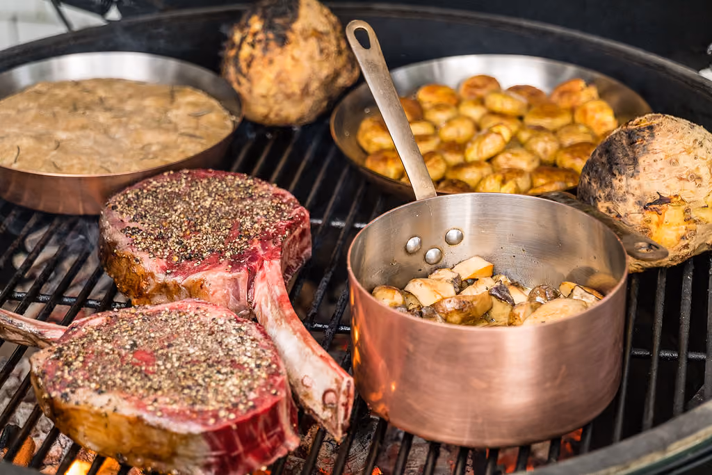 Steaks, celery root, and mushrooms cooking on an outdoor grill