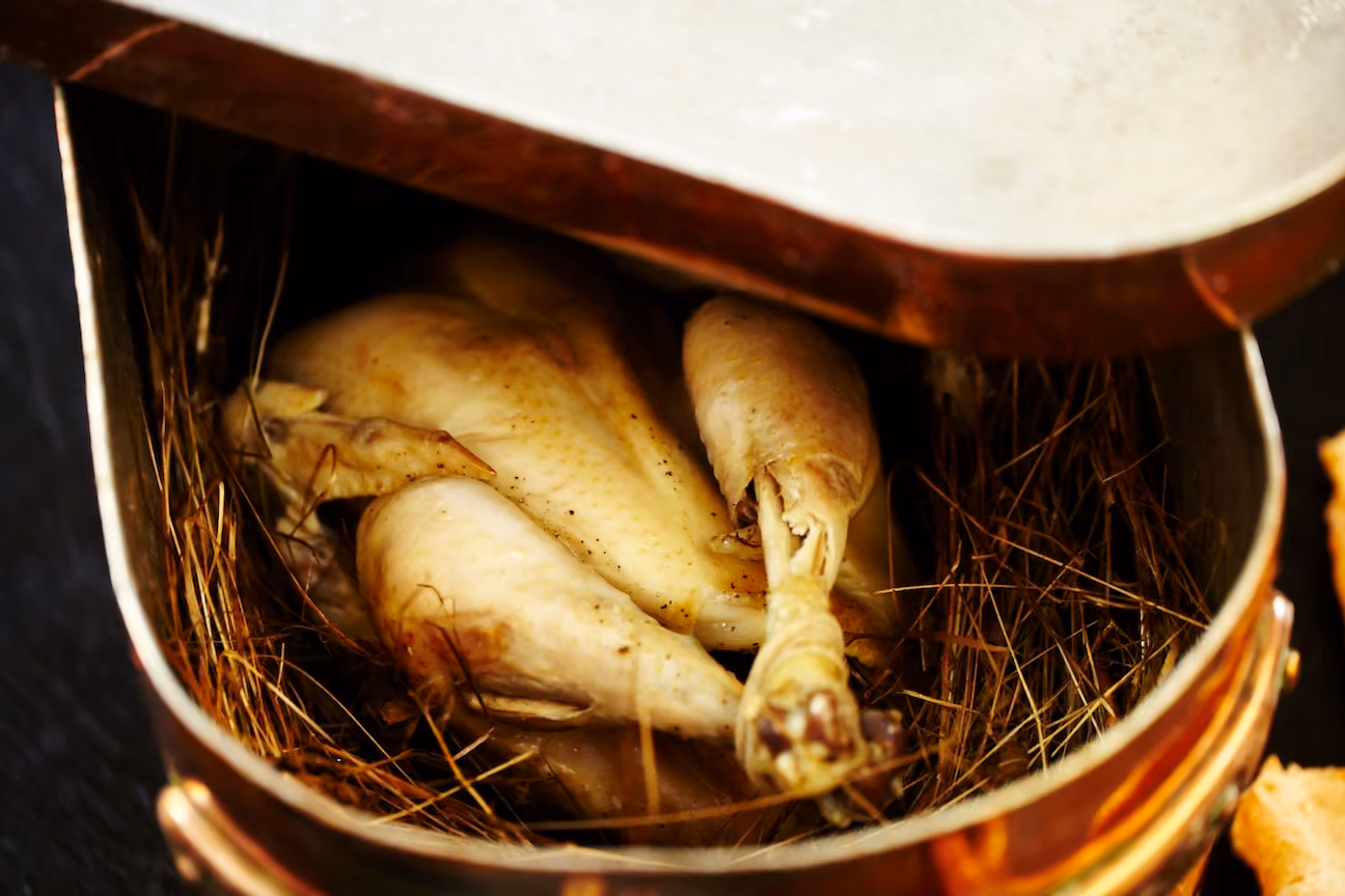 Roasted whole quail nestled in hay inside a copper pot