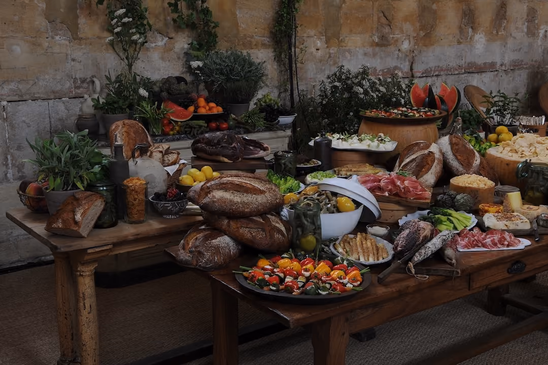 Large outdoor rustic spread of breads, cured meats, cheeses, fruit, and vegetables on a wooden table
