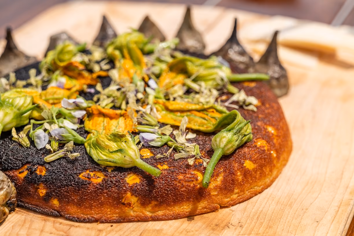 Overhead view of a charred flatbread topped with squash blossoms and edible flowers