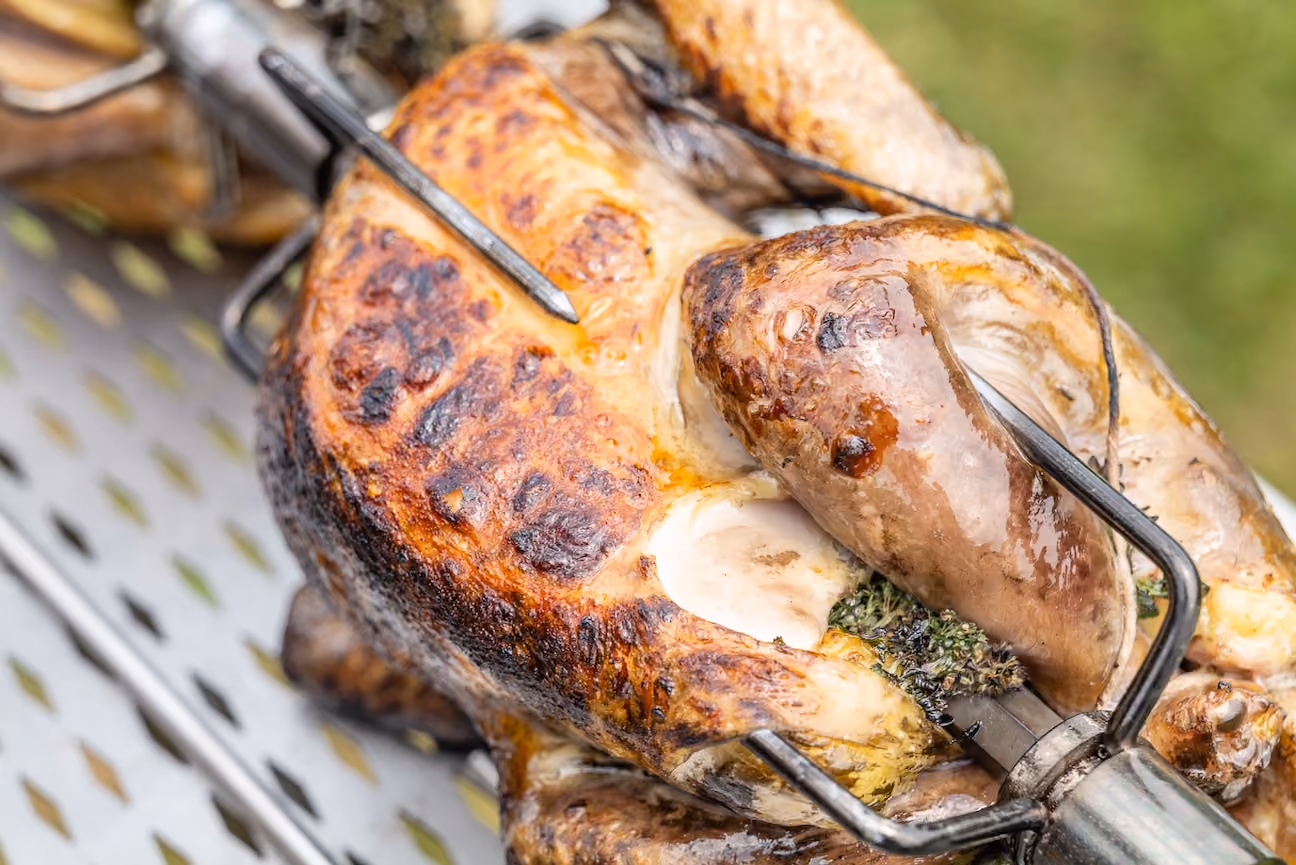 Close-up of a whole chicken roasting on a rotisserie spit