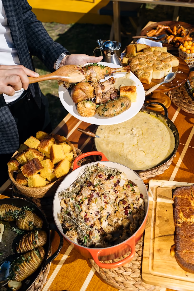 Overhead outdoor scene of a person serving roasted meat and sides from a buffet table