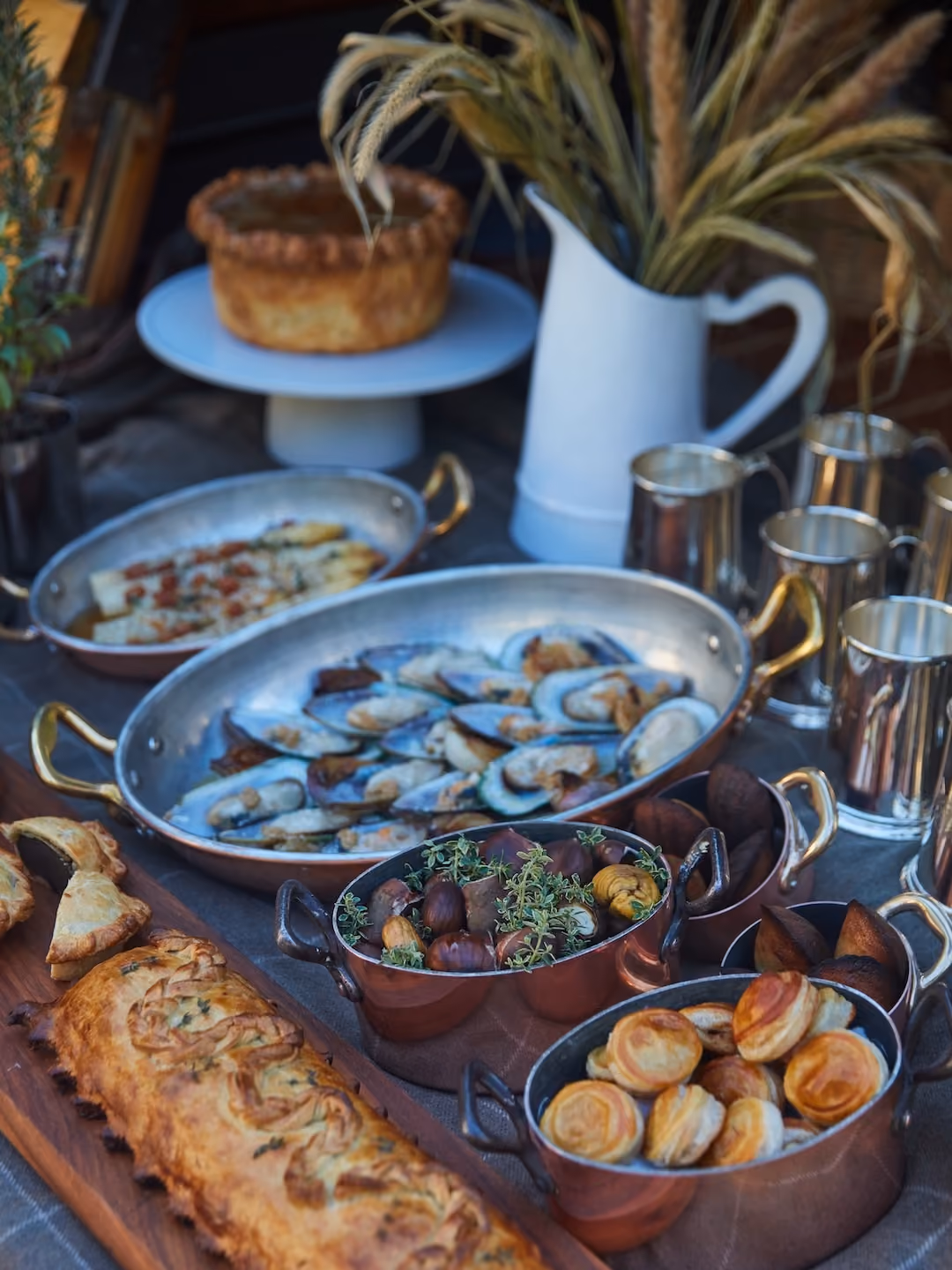 Outdoor buffet spread with mussels, a meat pie, roasted chestnuts, and puff pastry bites