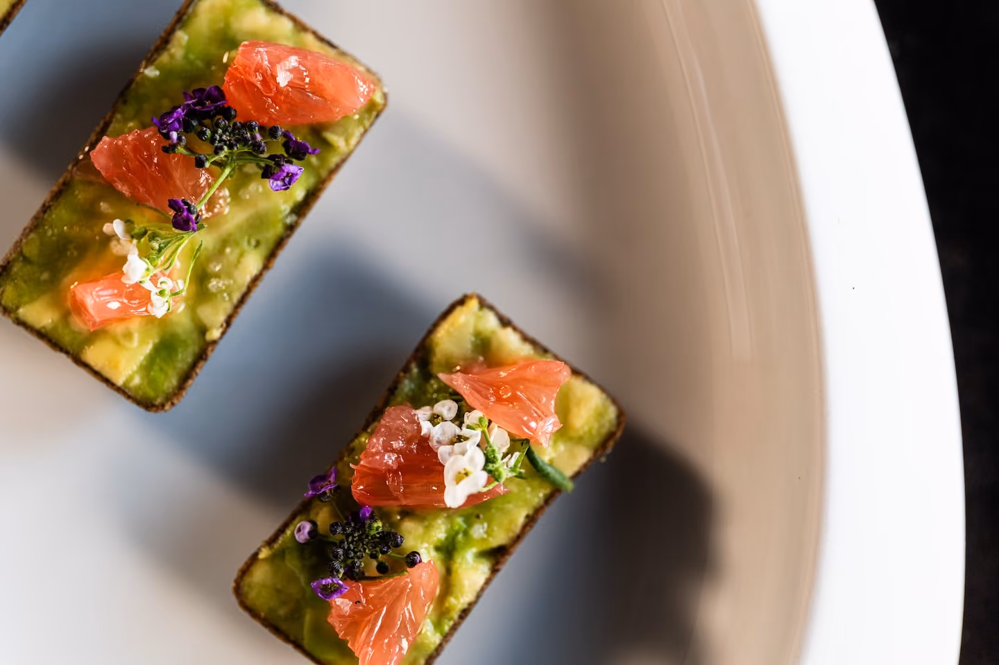 Overhead view of avocado toast canapés topped with grapefruit, caviar, and edible flowers