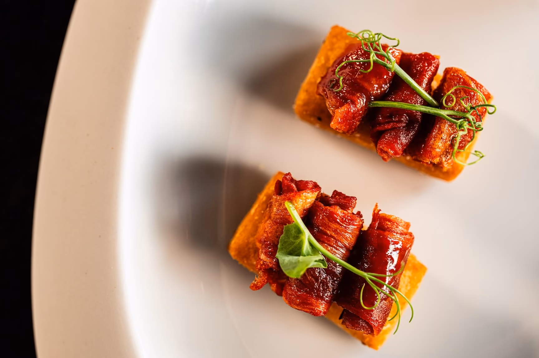 Glazed pork belly bites on fried polenta squares garnished with pea tendrils