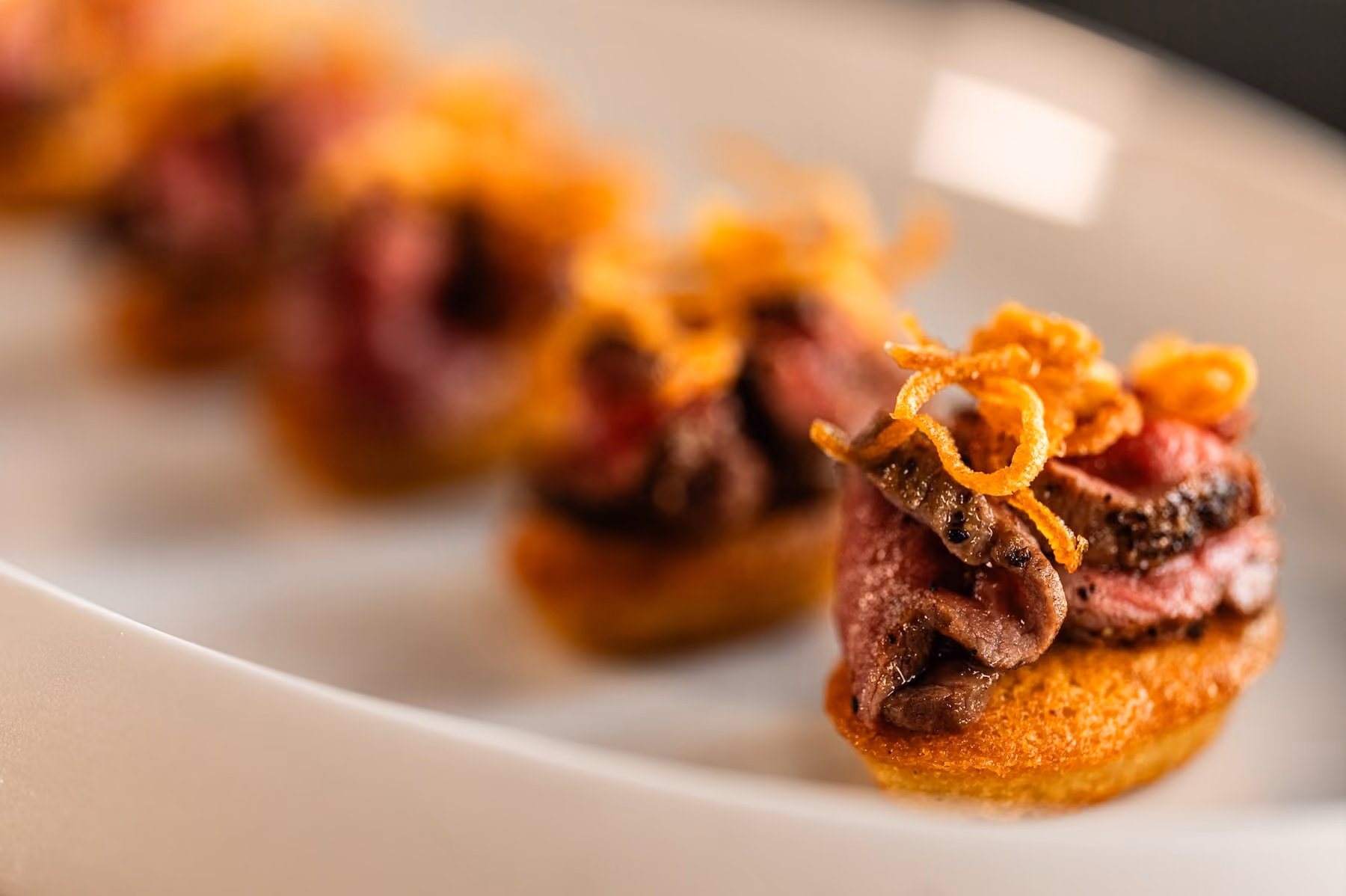 Row of seared beef canapés topped with crispy fried shallots
