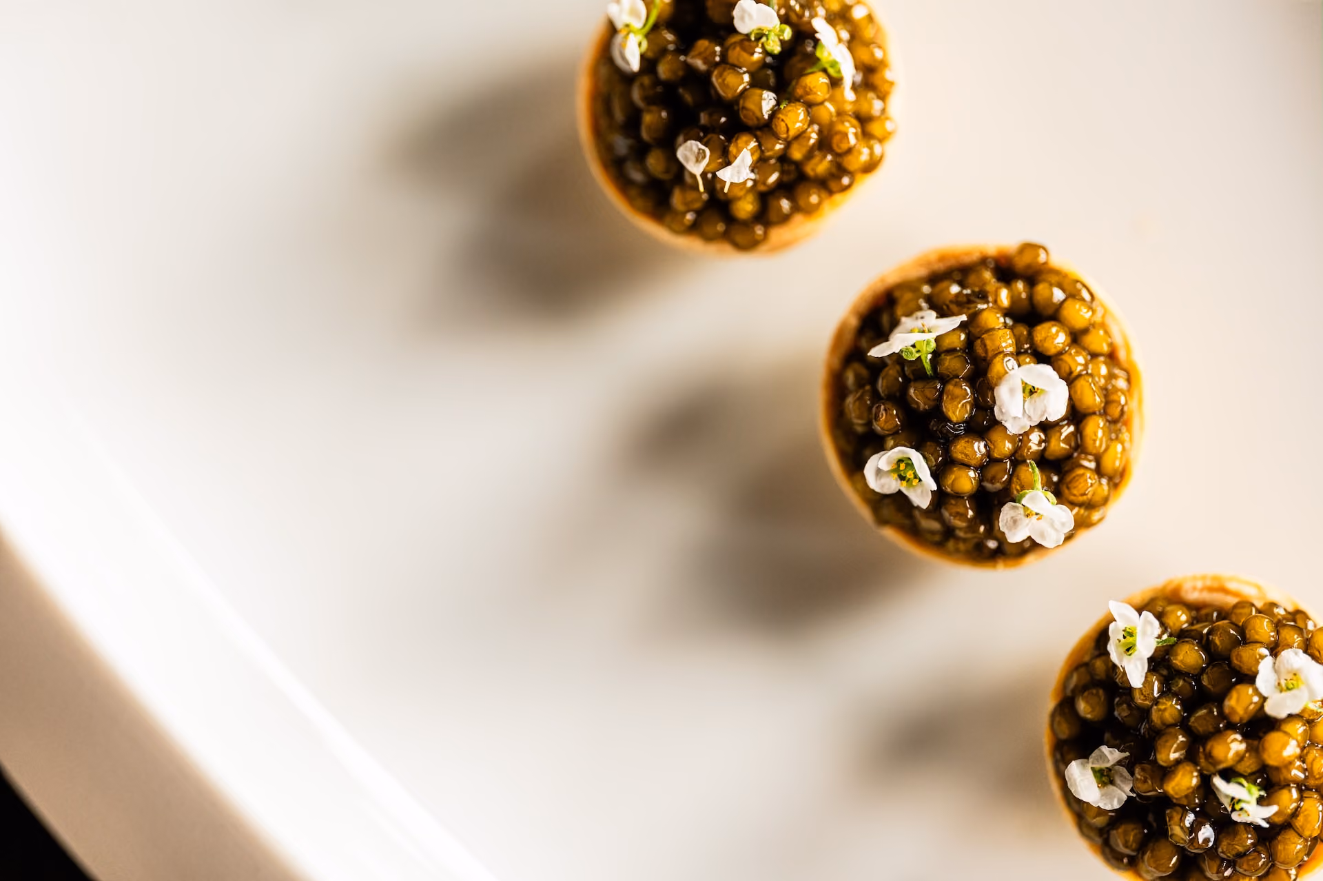 Overhead view of tartlets topped with black caviar and white flowers