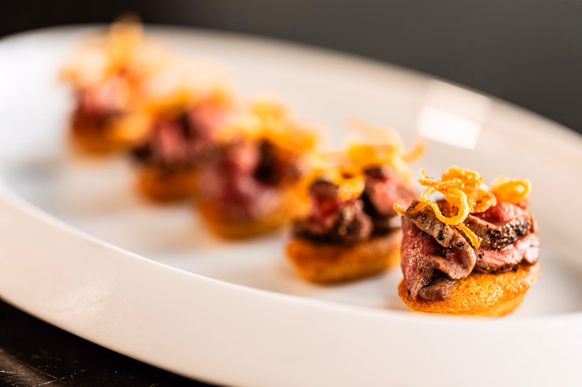 Row of seared beef canapés on toast topped with crispy fried shallots