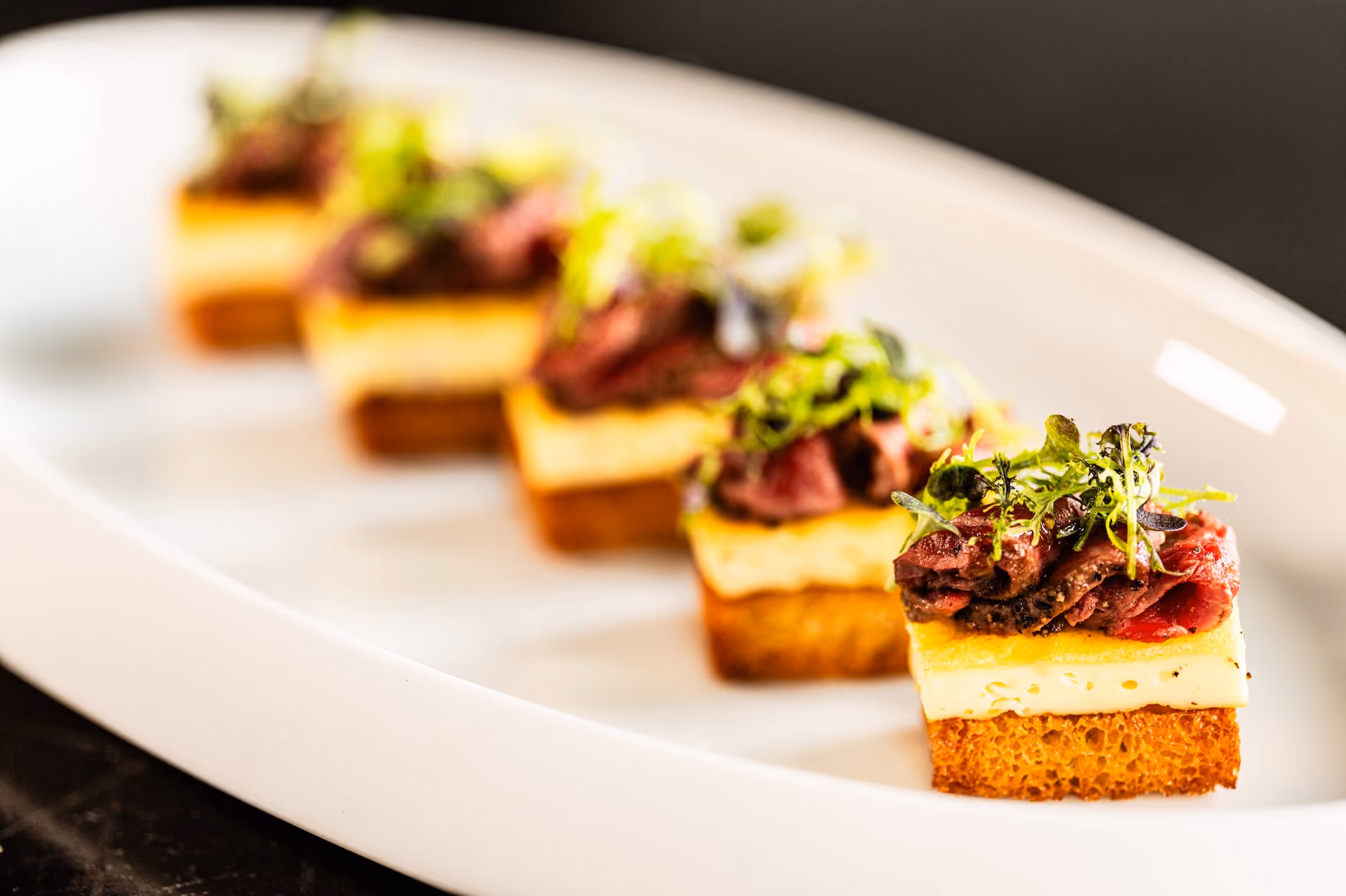 Row of canapés with beef, cheese, and frisée on toasted brioche