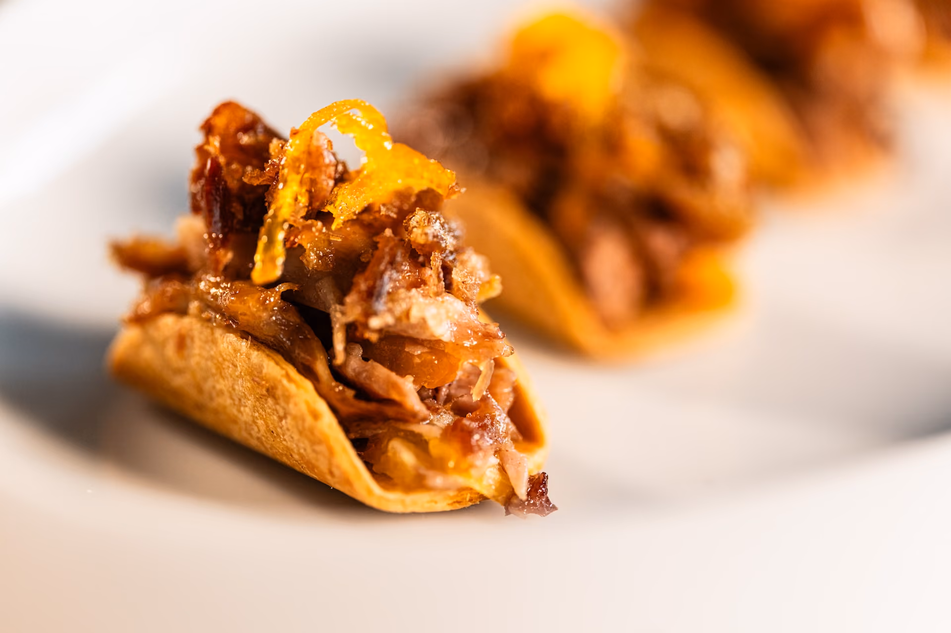 Taco-shaped canapé filled with crispy pulled meat and citrus zest garnish