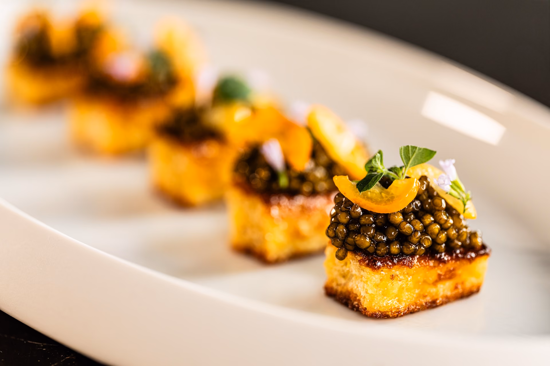 Row of crostini topped with black caviar, candied citrus, and herb flowers