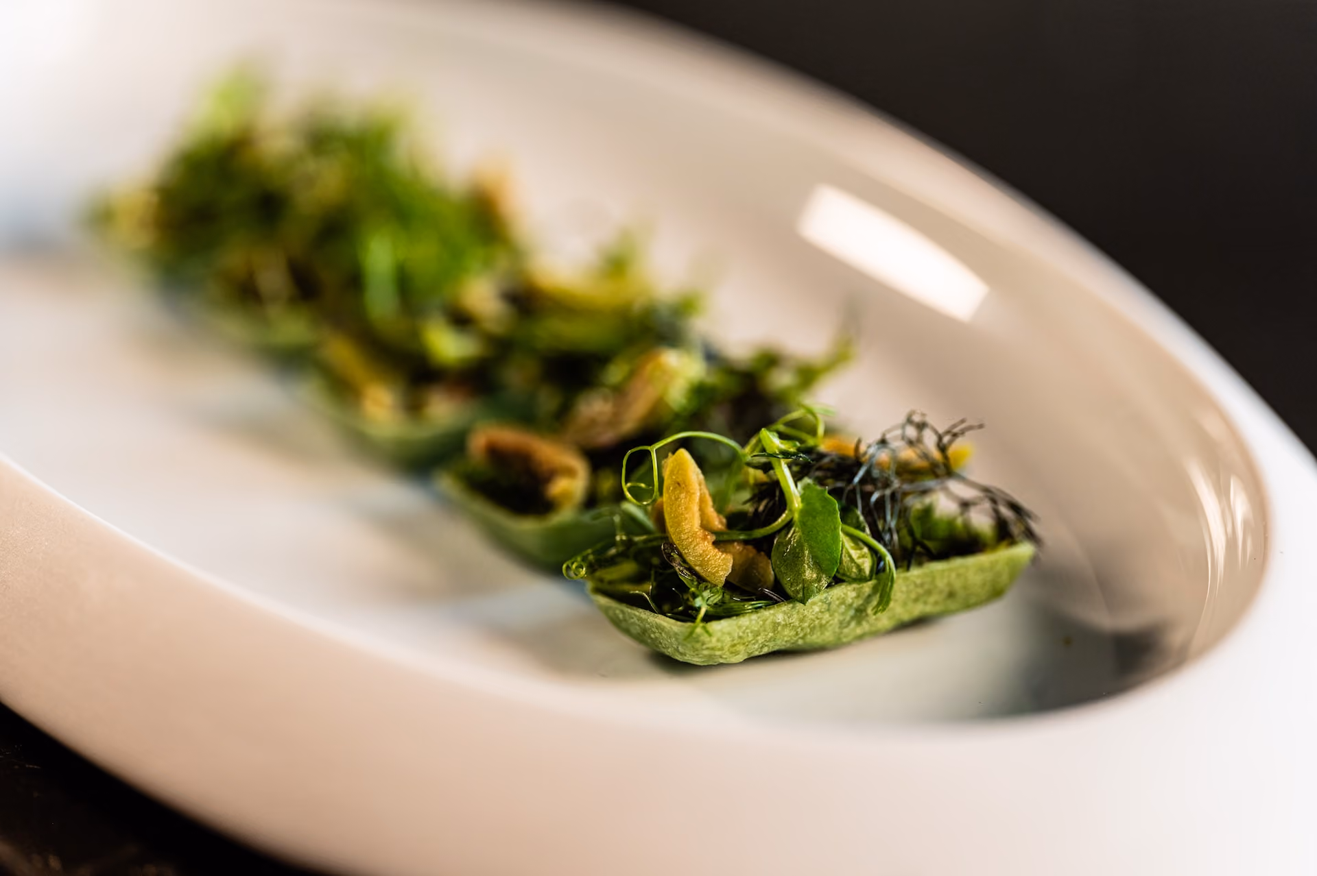 Row of green tartlet boats topped with herbs, greens, and a crispy garnish