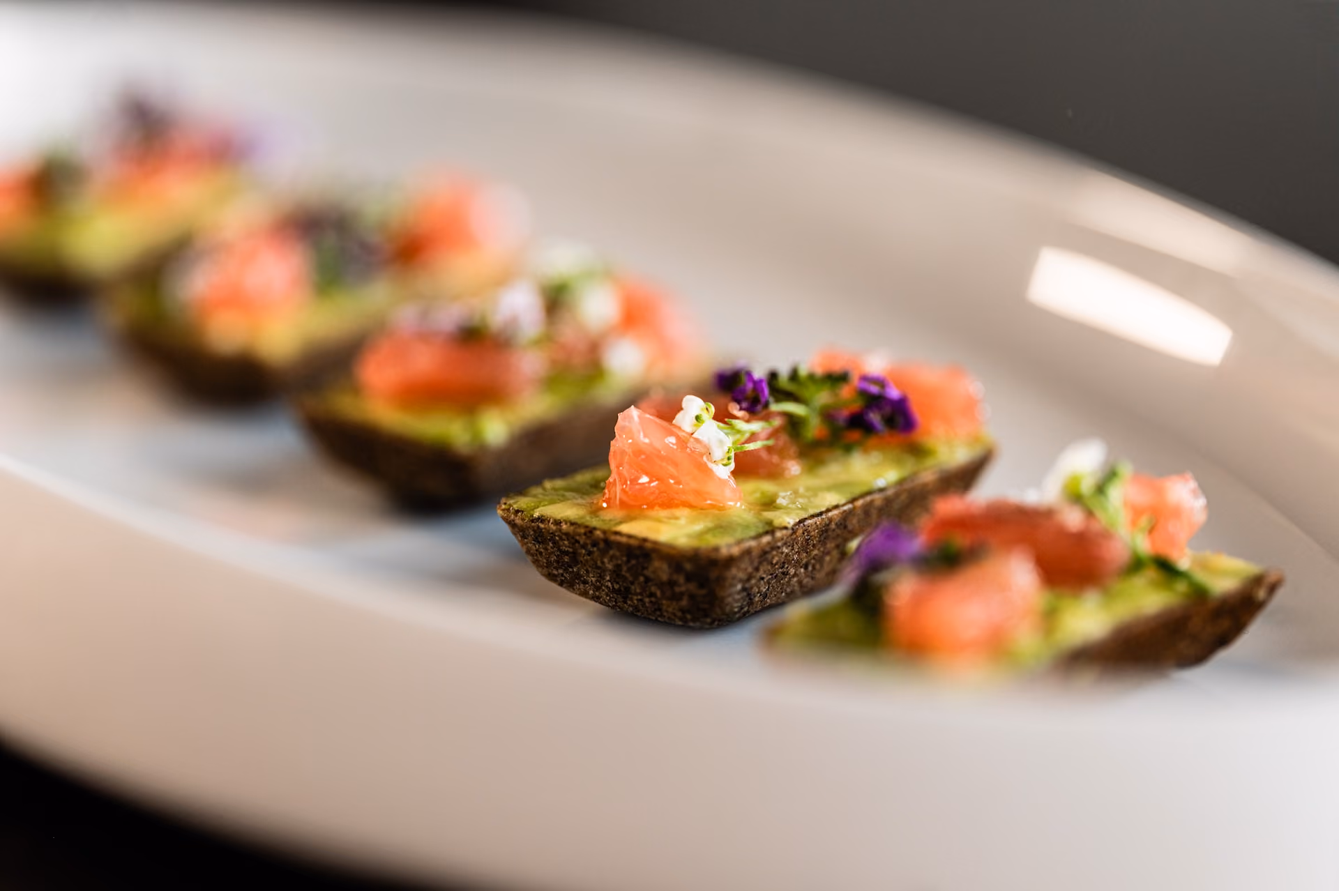 Pumpernickel toast canapés topped with avocado, salmon, and edible flowers
