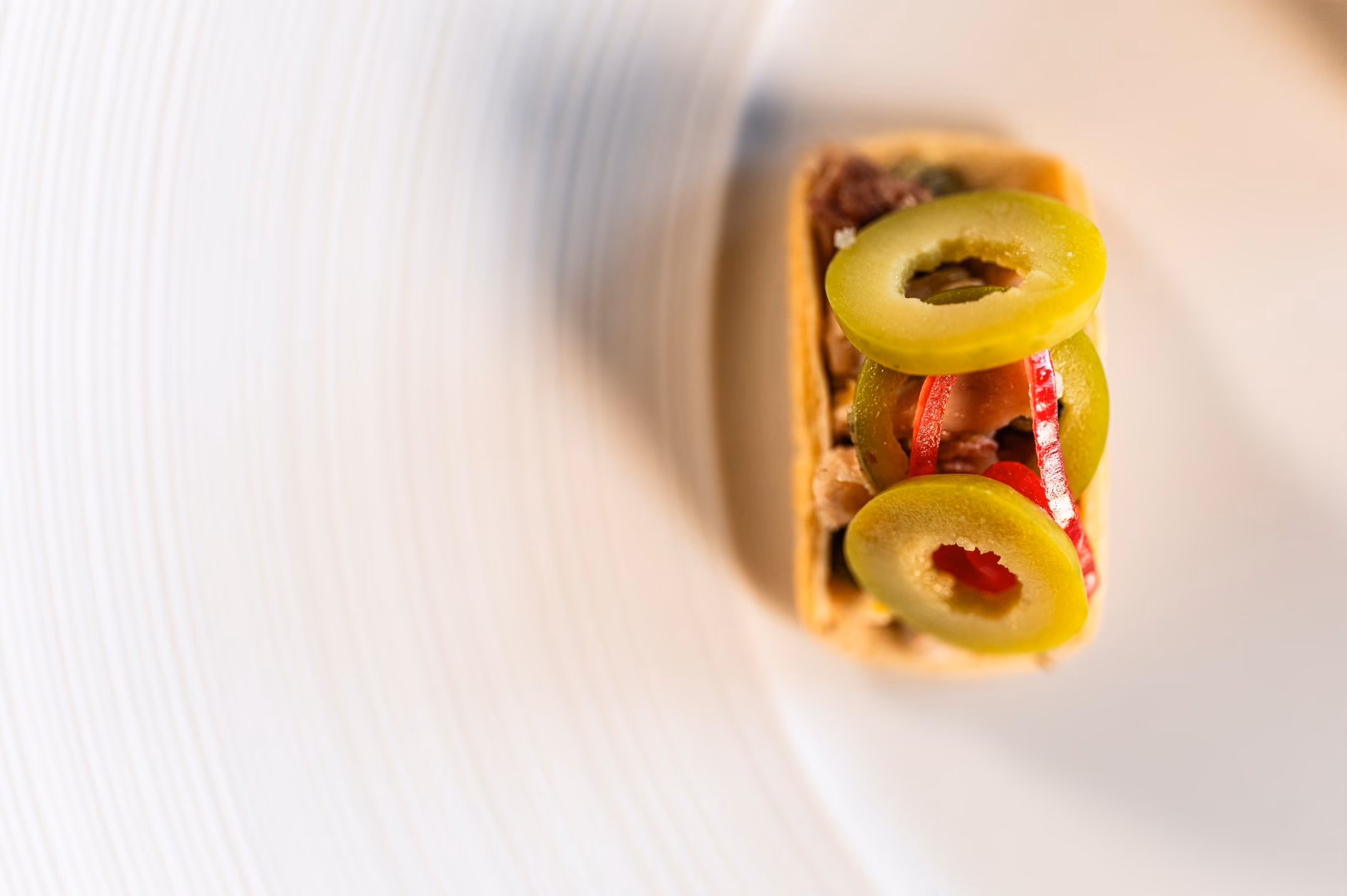 Overhead view of a taco-shaped canapé topped with green olive slices and red pepper