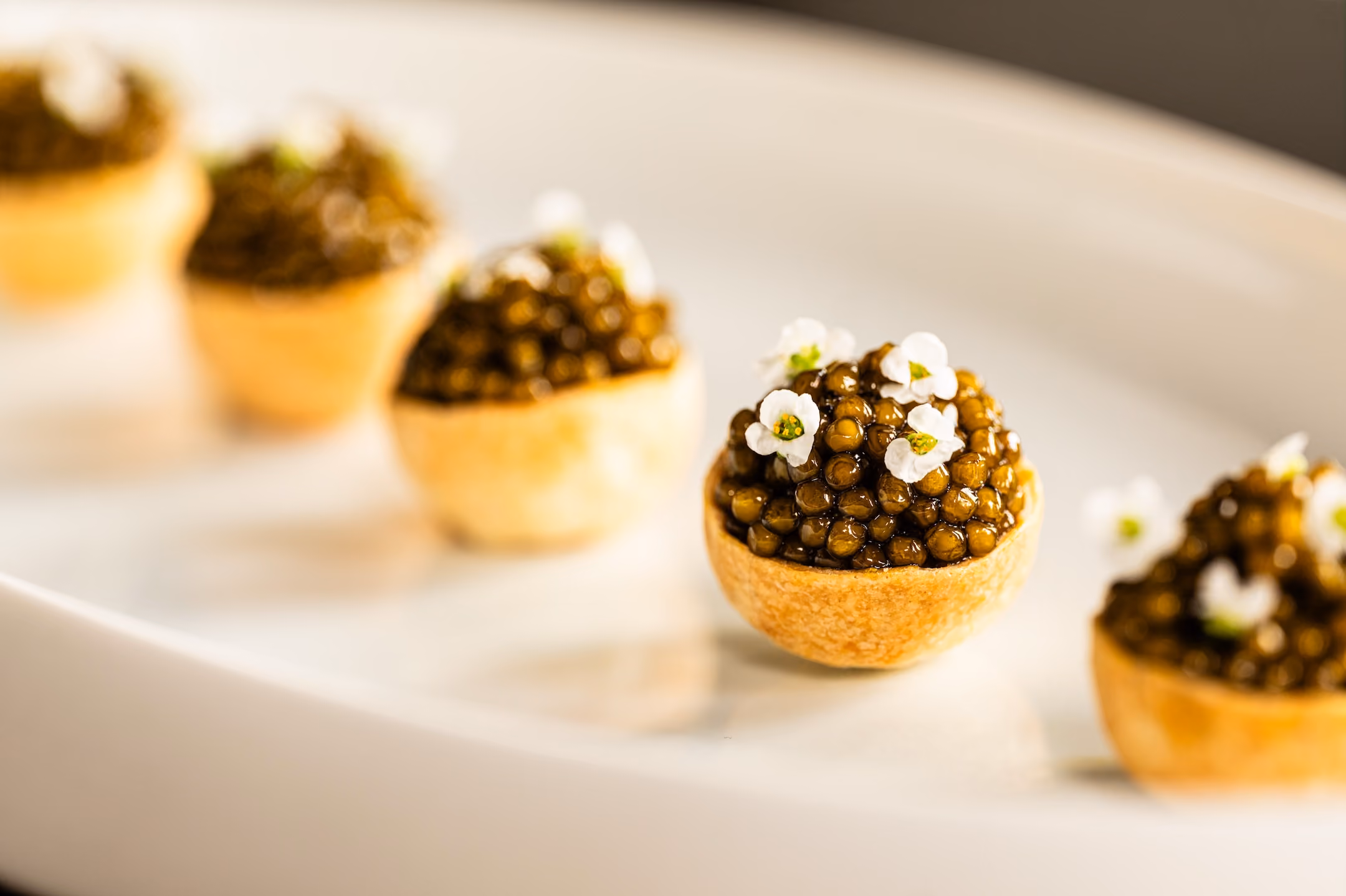 Tartlets topped with caviar and white flowers, arranged on a white plate