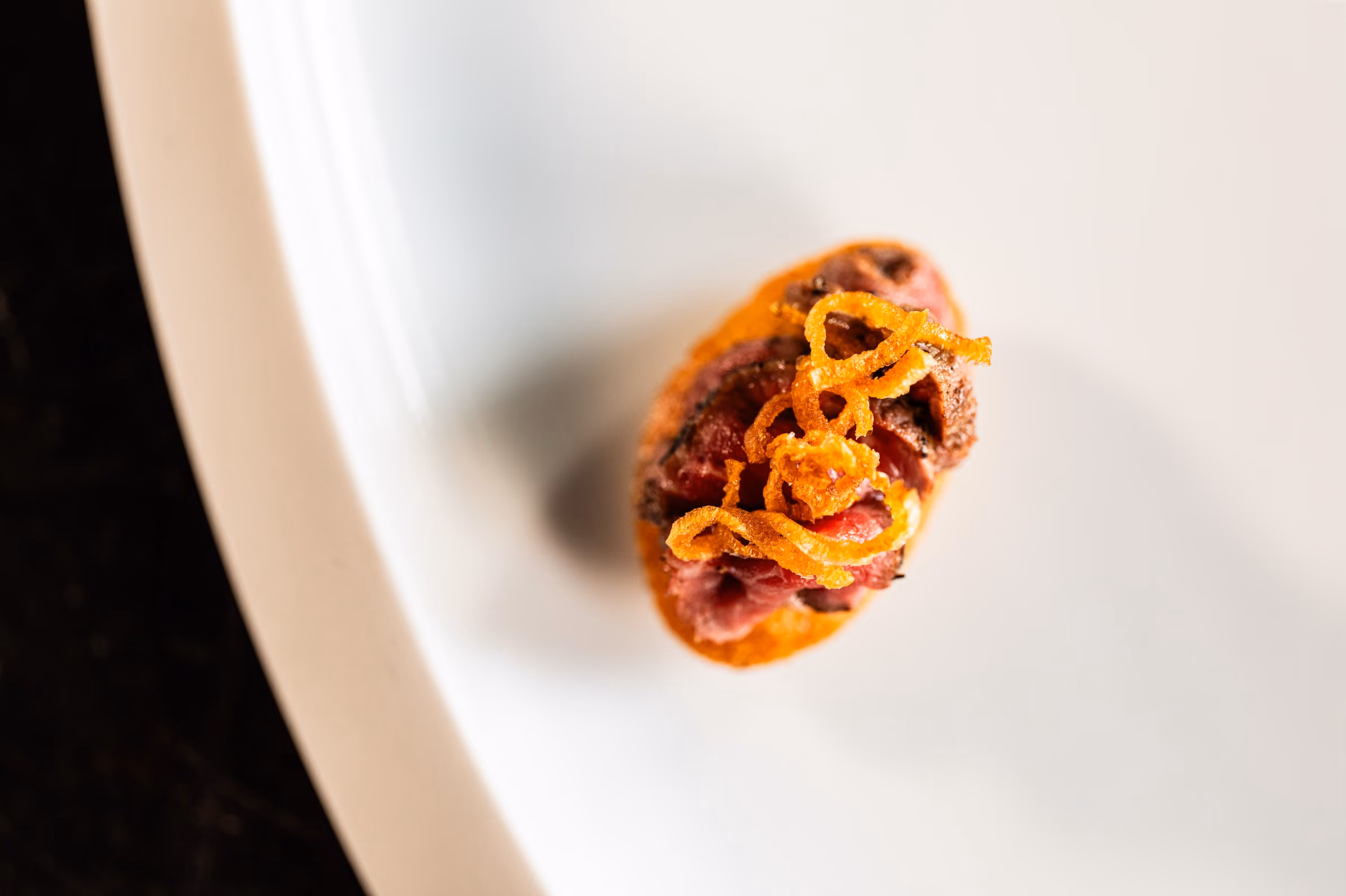 Overhead view of a seared beef canapé topped with crispy fried shallots