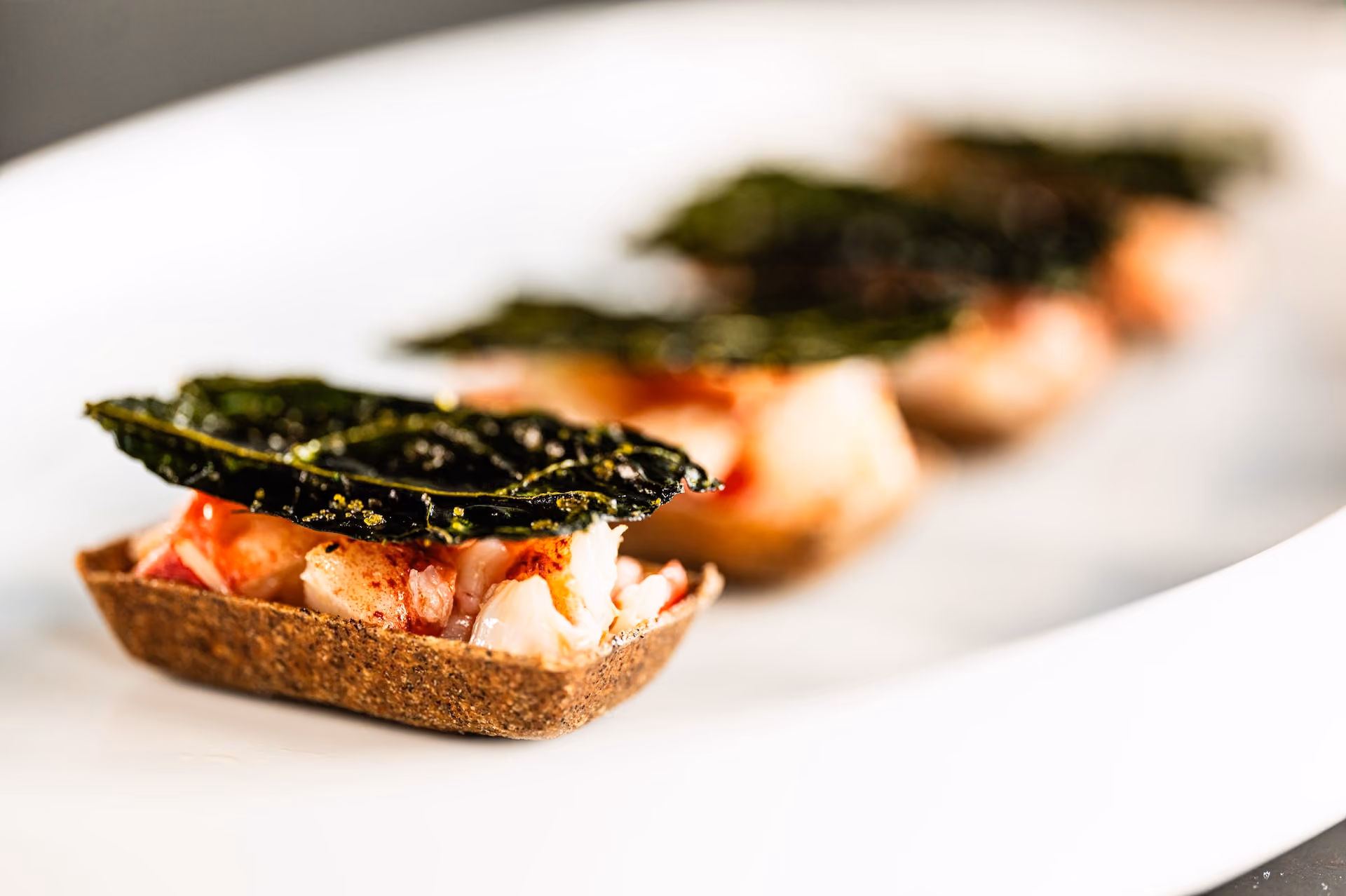 Crab canapés in dark rye tart shells topped with crispy kale chips