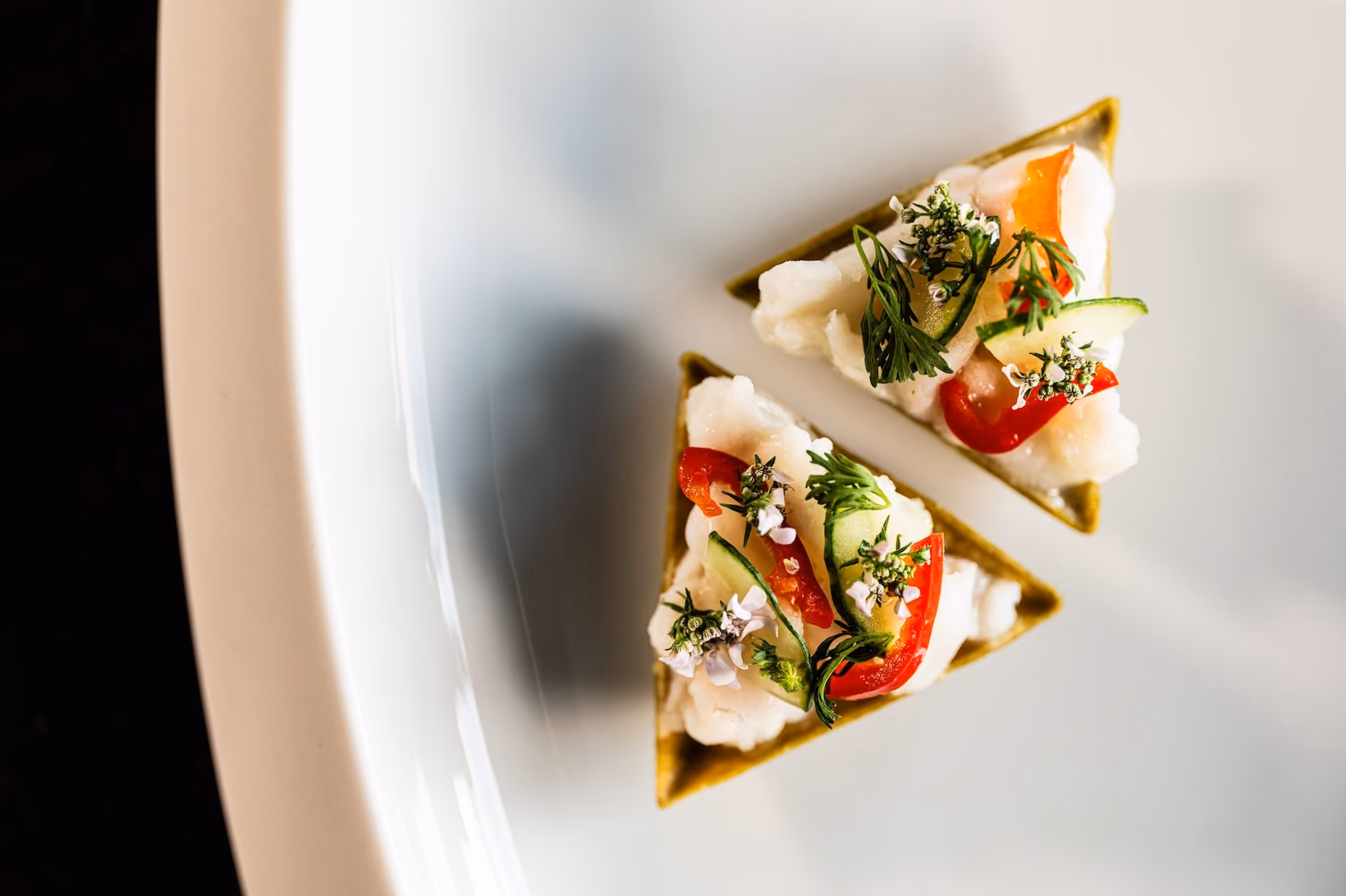Triangular green tartlets topped with fish, cucumber, tomato, and herb flowers
