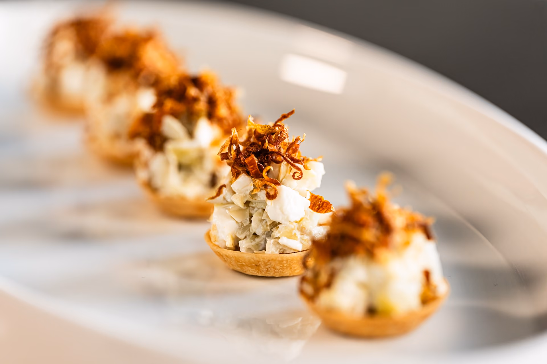 Row of tartlet canapés topped with a creamy salad and crispy fried shallots