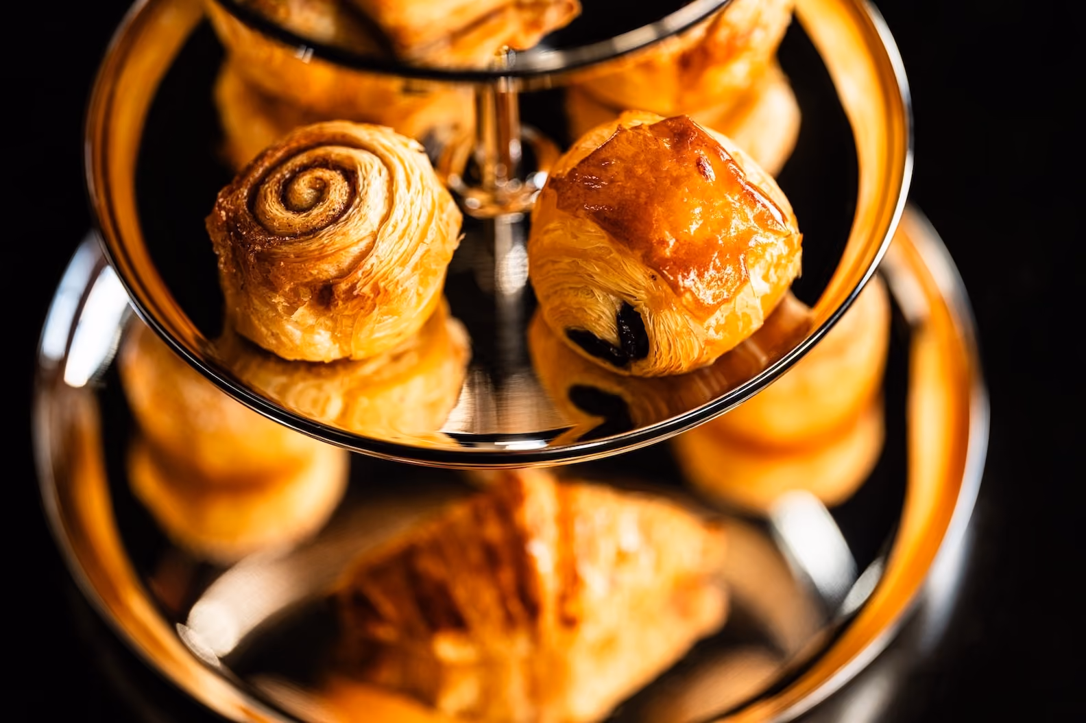 Close-up of pastries on a tiered stand, including a cinnamon roll and chocolate croissant
