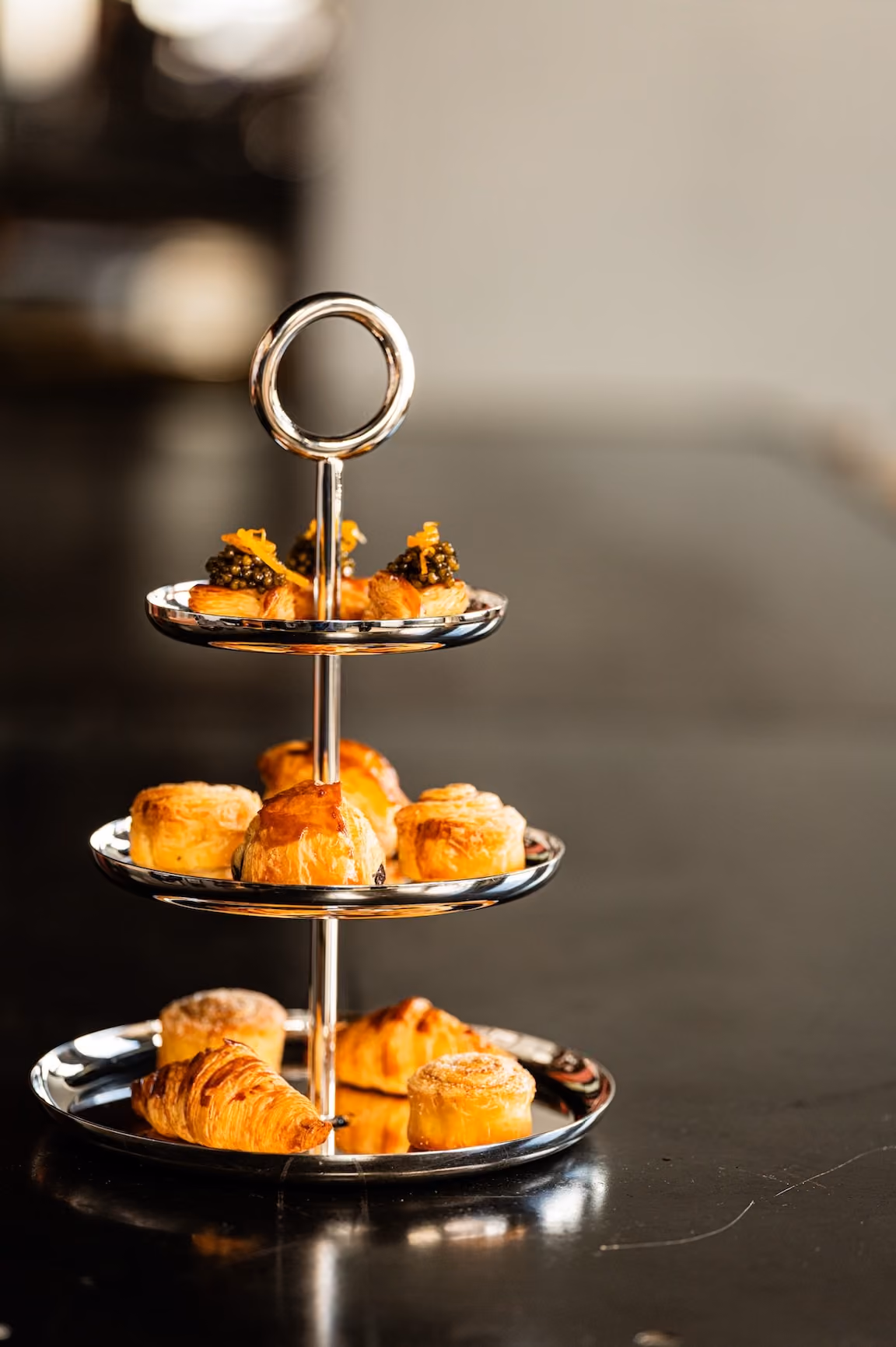 Three-tier silver stand displaying assorted canapés and pastries