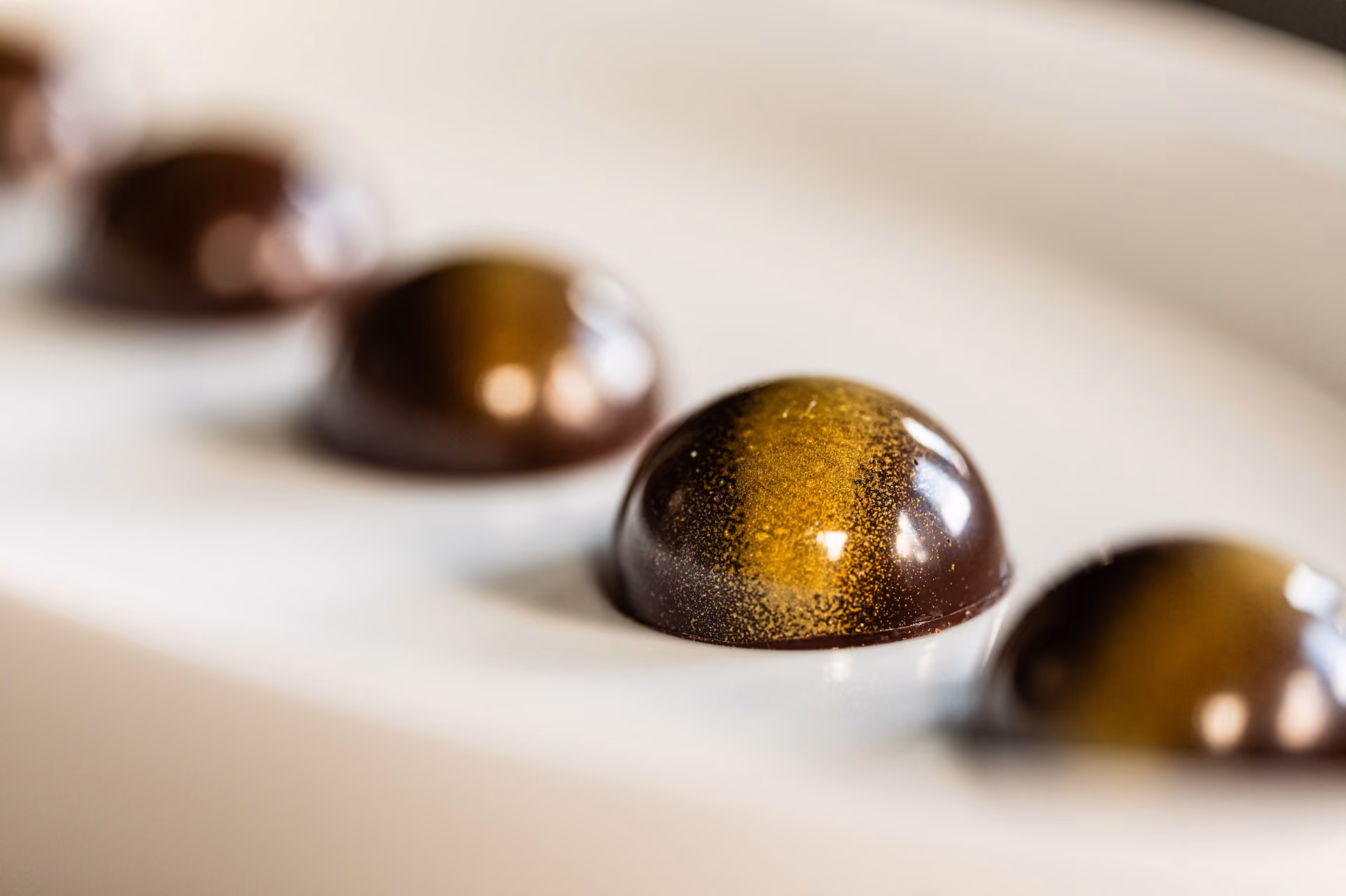 Row of dark chocolate dome bonbons dusted with gold shimmer