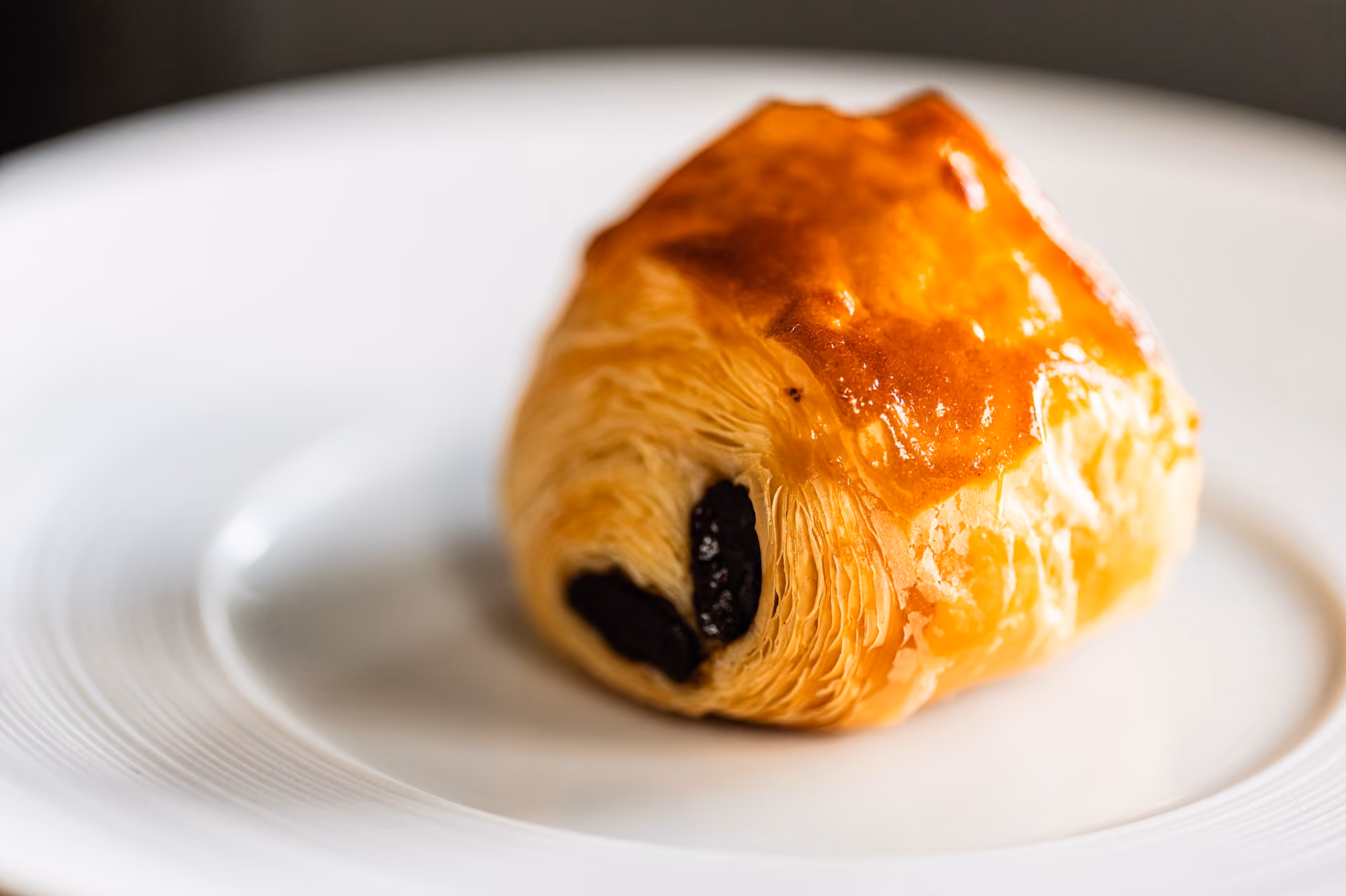 Glazed pain au chocolat pastry with dark chocolate filling on a white plate
