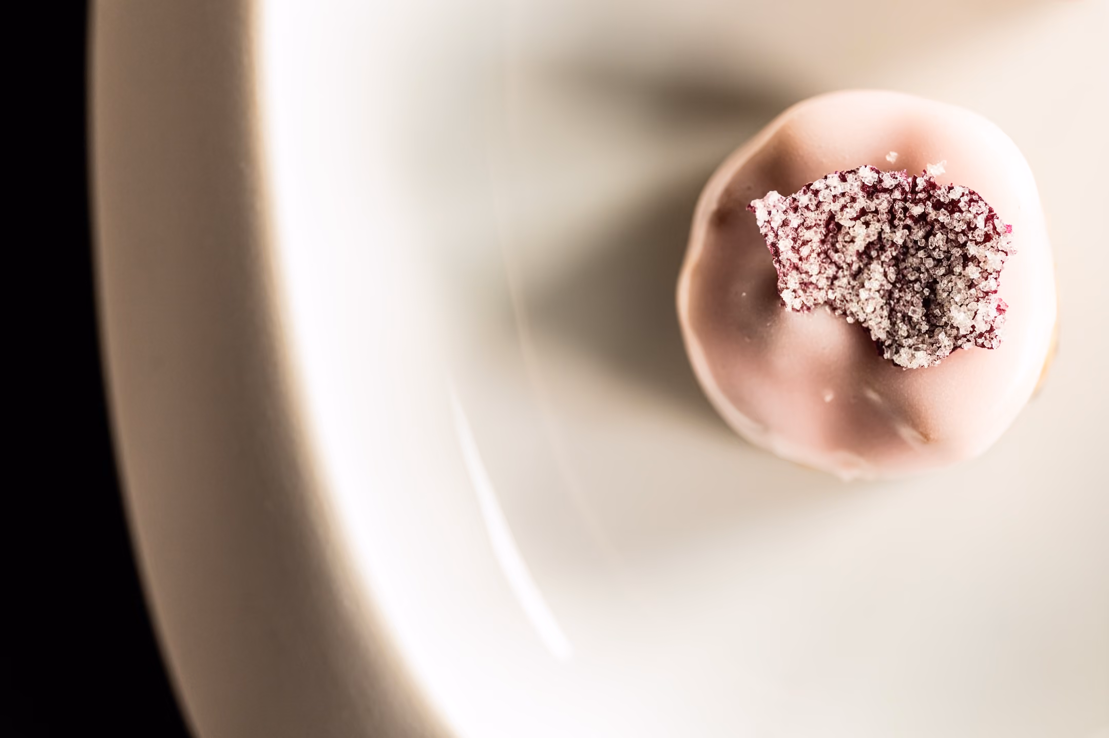 Overhead close-up of a pink-glazed petit four topped with dried berries and sugar crystals