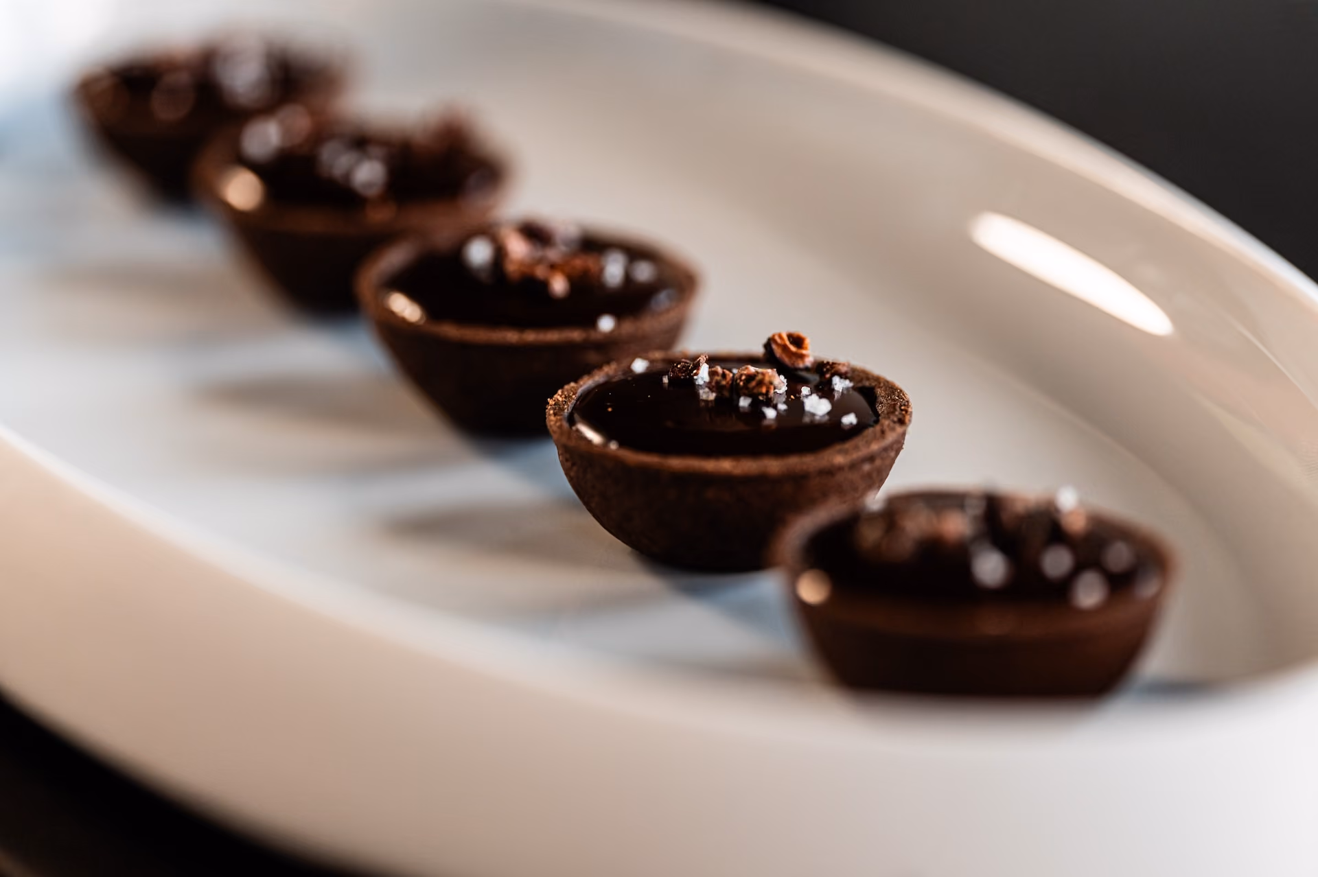 Chocolate tartlets with glossy ganache topped with cacao nibs and sea salt flakes