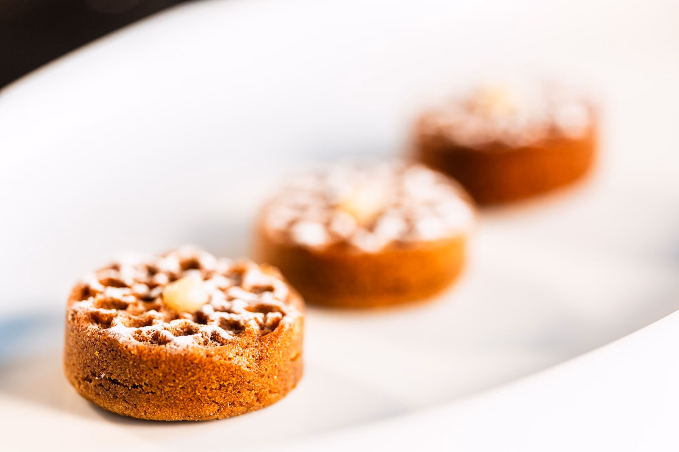 Three round spiced financier cakes with lattice sugar-dusted tops on a white plate