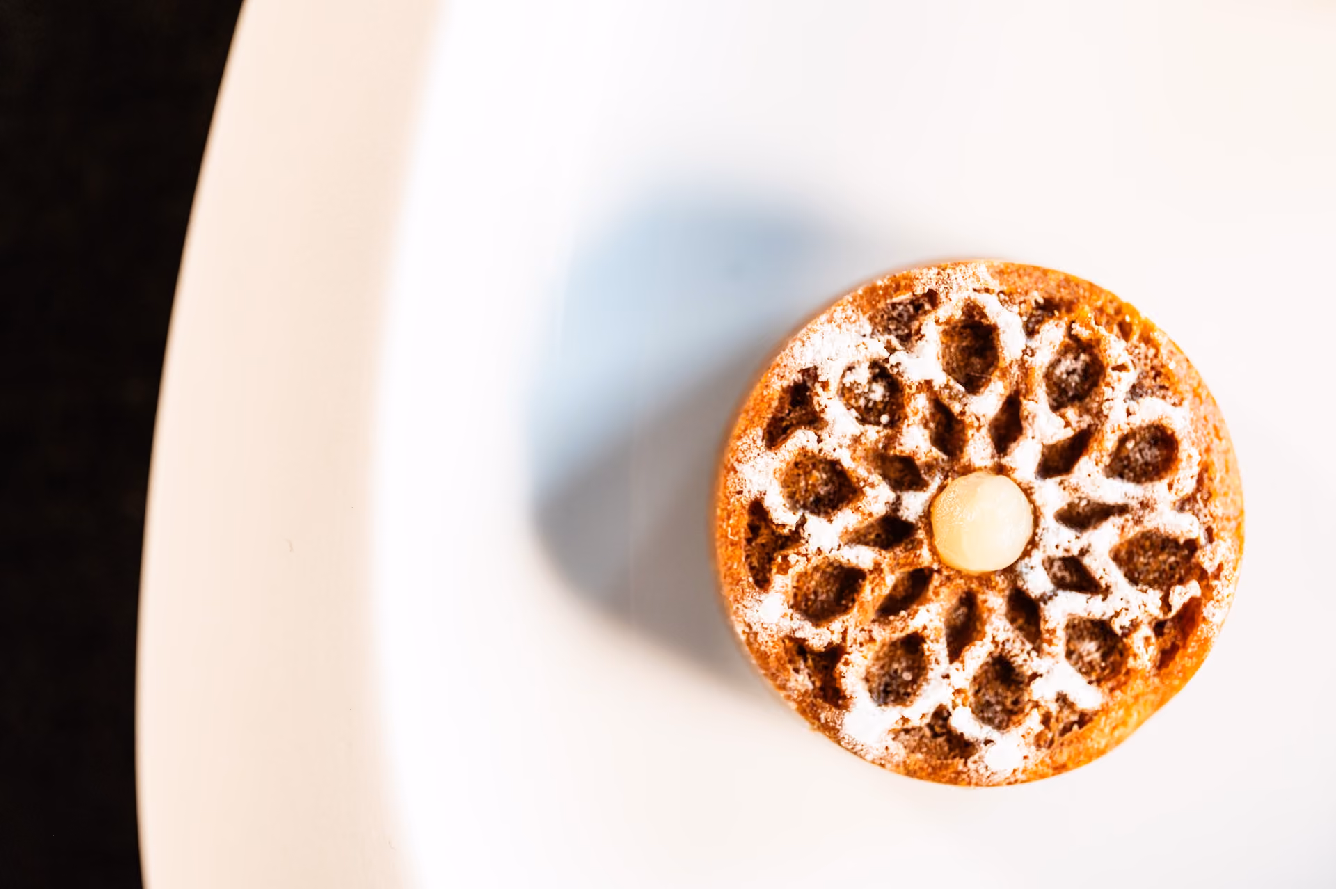 Overhead view of a round spiced financier cake with a lattice glaze pattern and powdered sugar