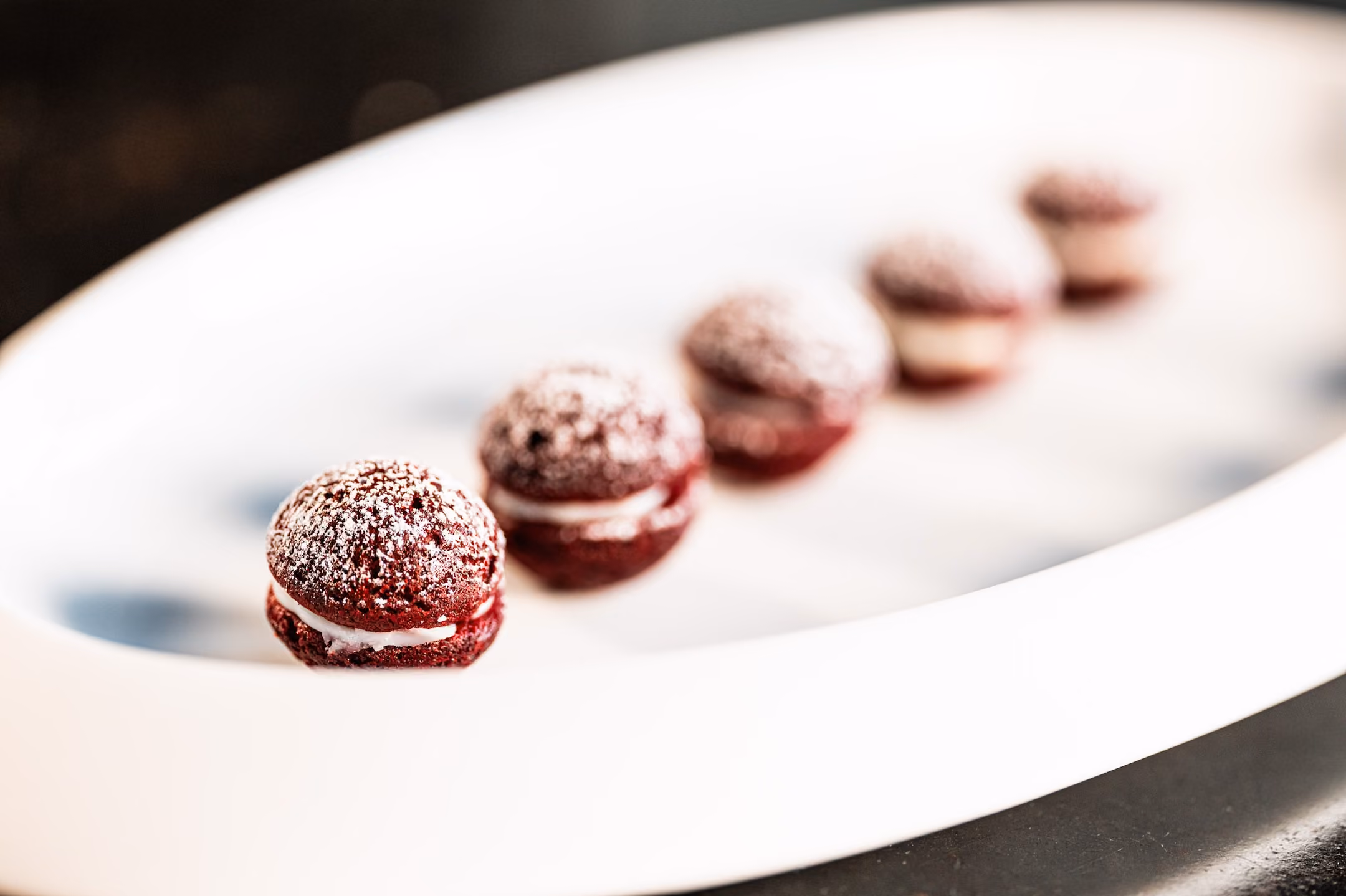 Row of red velvet whoopie pies dusted with powdered sugar on a white oval plate