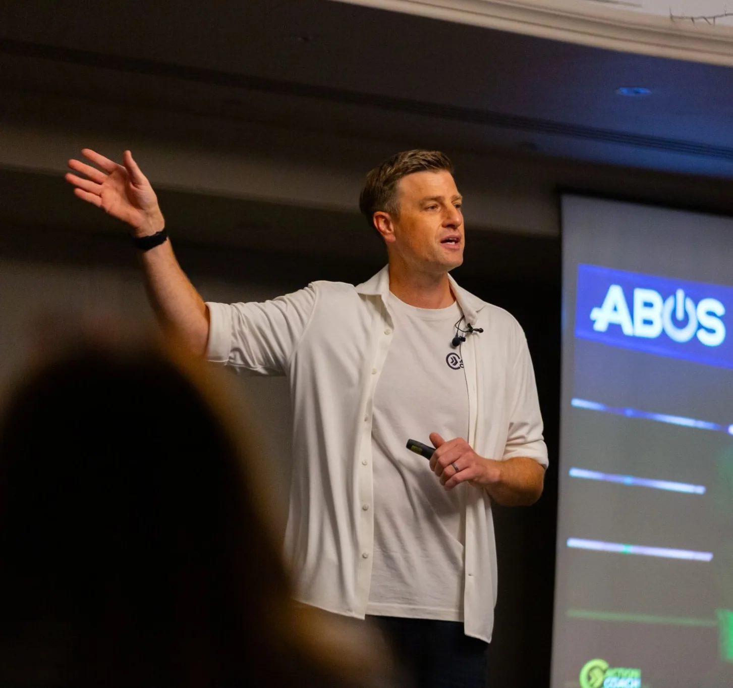 James Vincent speaking at an ActionCOACH event, gesturing towards a presentation screen