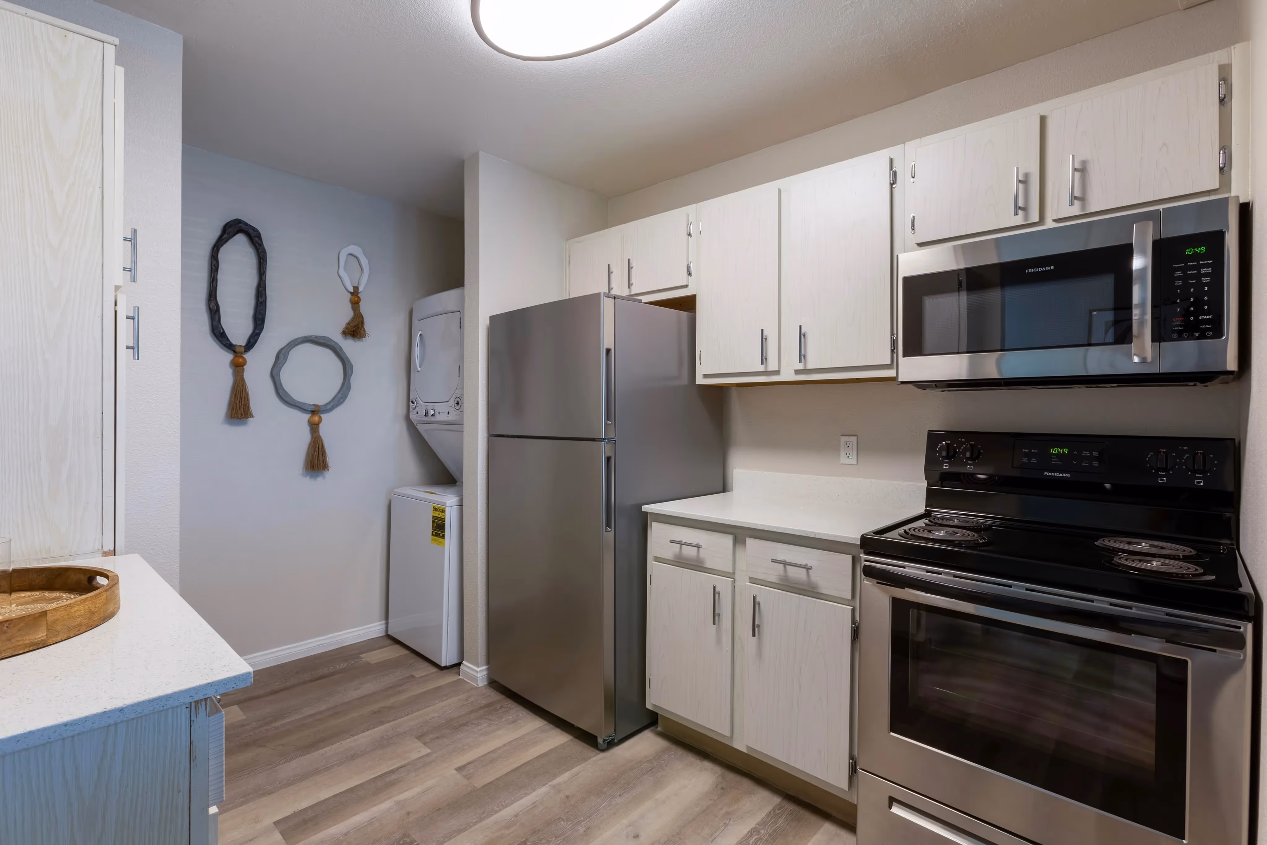 Apartment kitchen with white cabinetry, stainless steel appliances, and wood-look flooring, with a stacked washer/dryer in the background, at Ascension at Ironwood in Tucson, AZ.