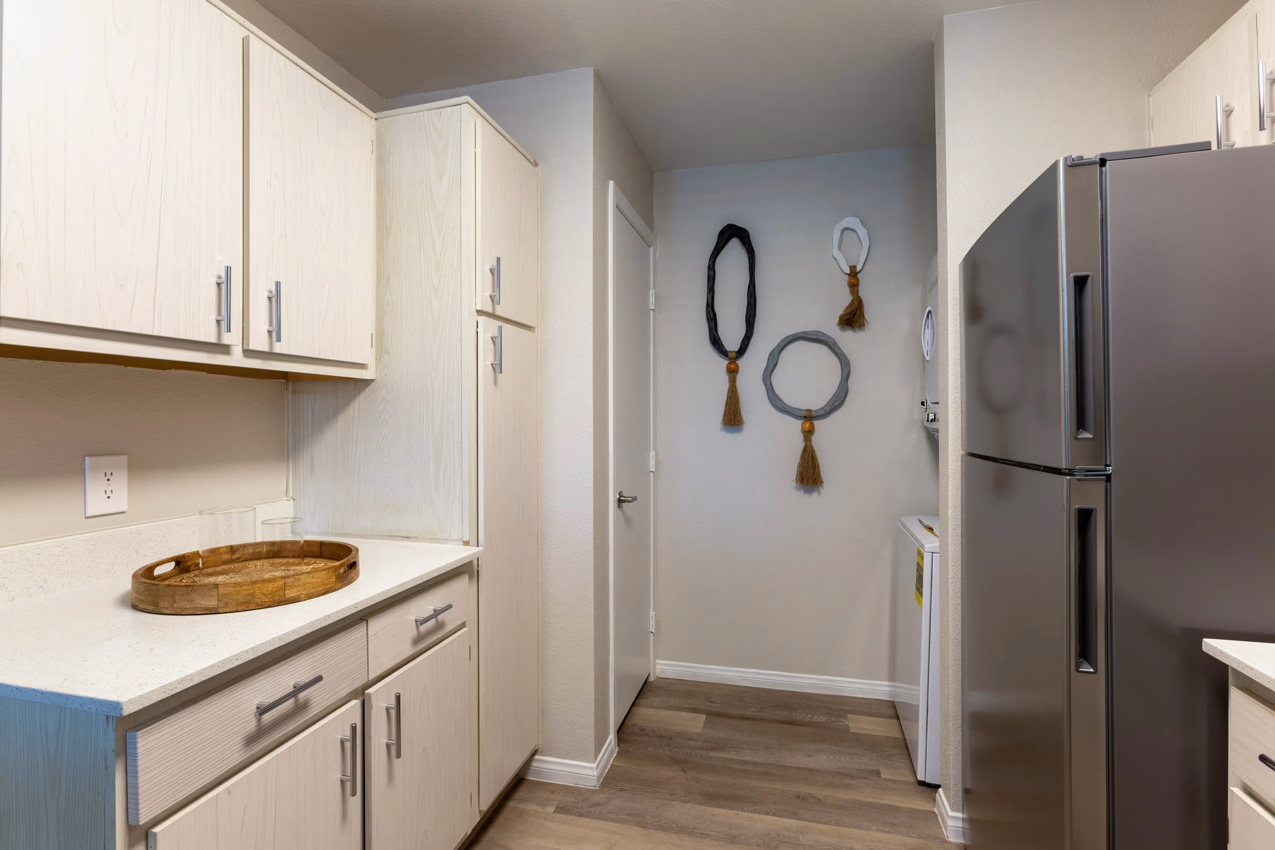 Apartment kitchen with white cabinetry and a stainless steel refrigerator, with a view of the in-unit laundry, at Ascension at Ironwood in Tucson, AZ.