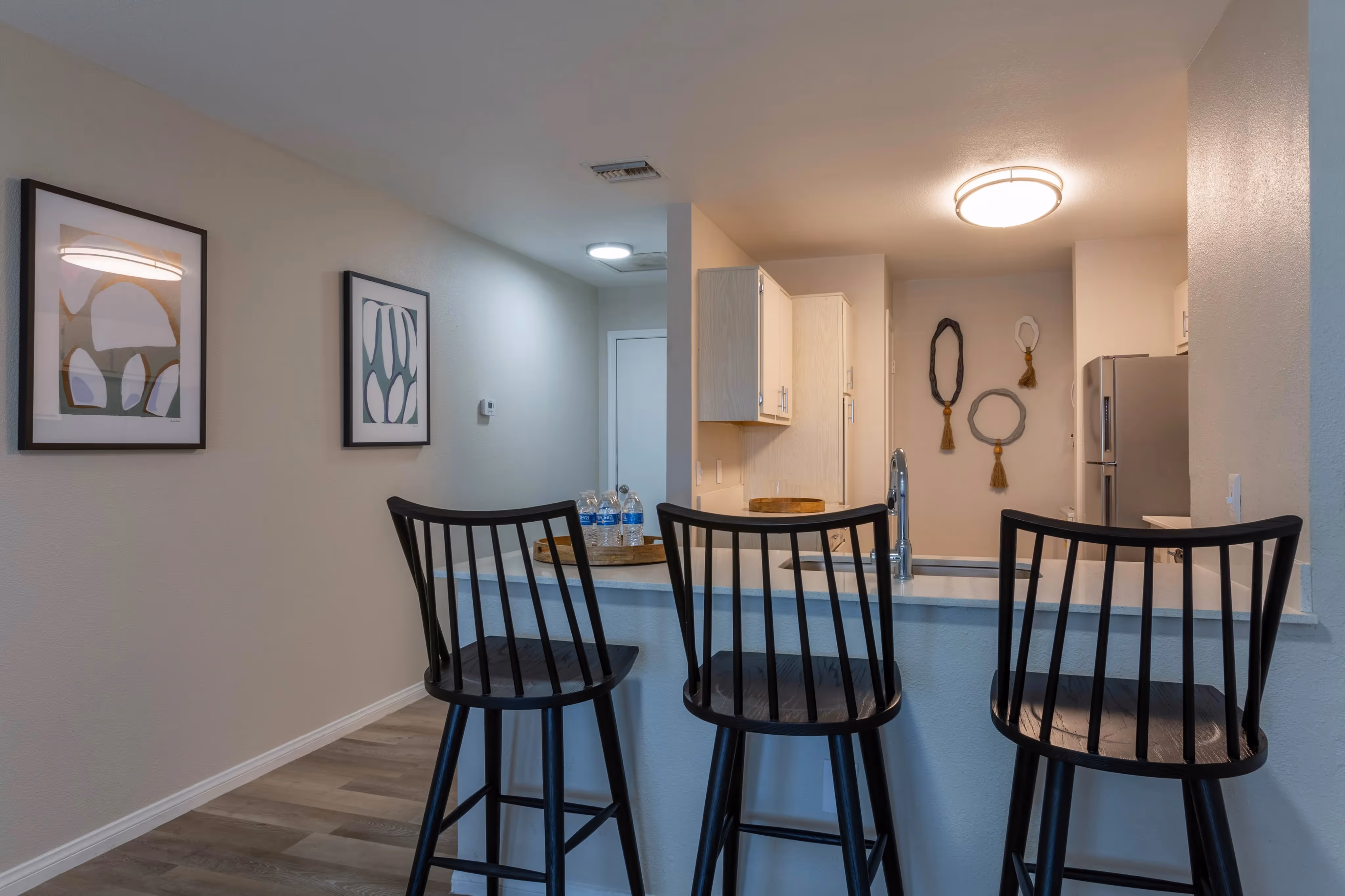Apartment kitchen with a breakfast bar and bar stools, and a view into the living area, at Ascension at Ironwood in Tucson, AZ.