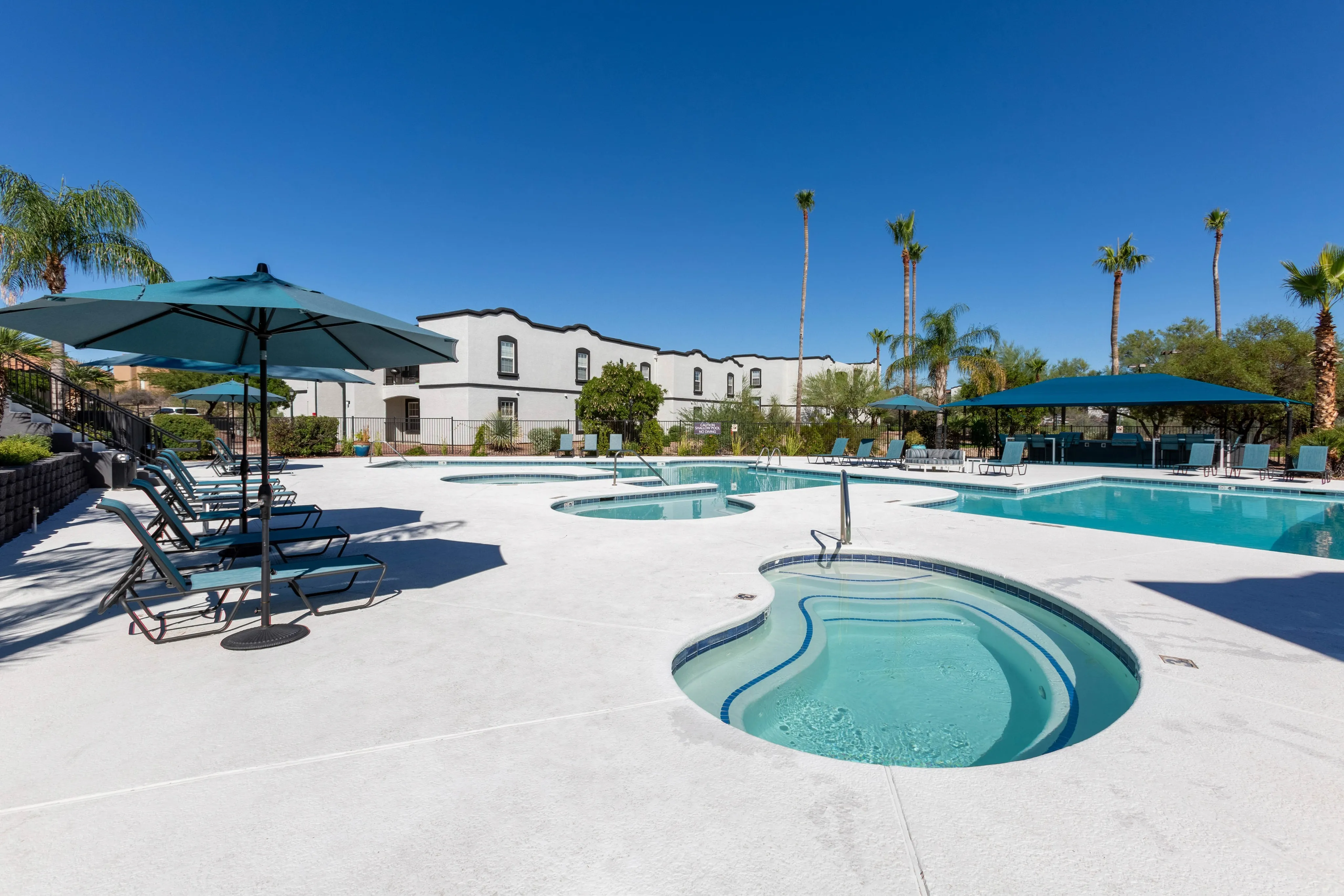 Resort-style swimming pool and hot tub area with a spacious sundeck and palm trees, a key amenity at Ascension at Ironwood in Tucson, AZ.