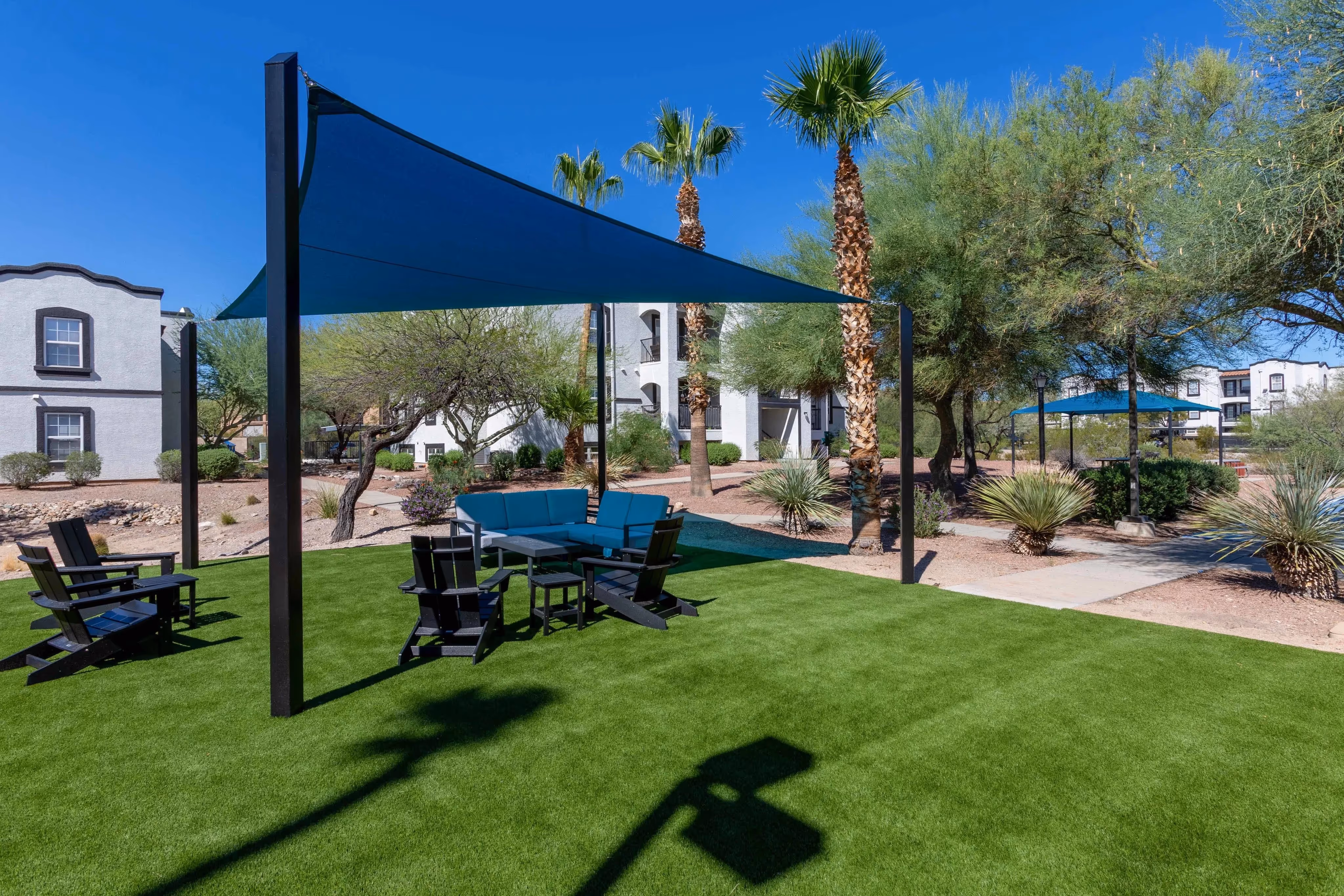 A green turf area with comfortable outdoor seating and shade sails, providing a community space at Ascension at Ironwood in Tucson, AZ.