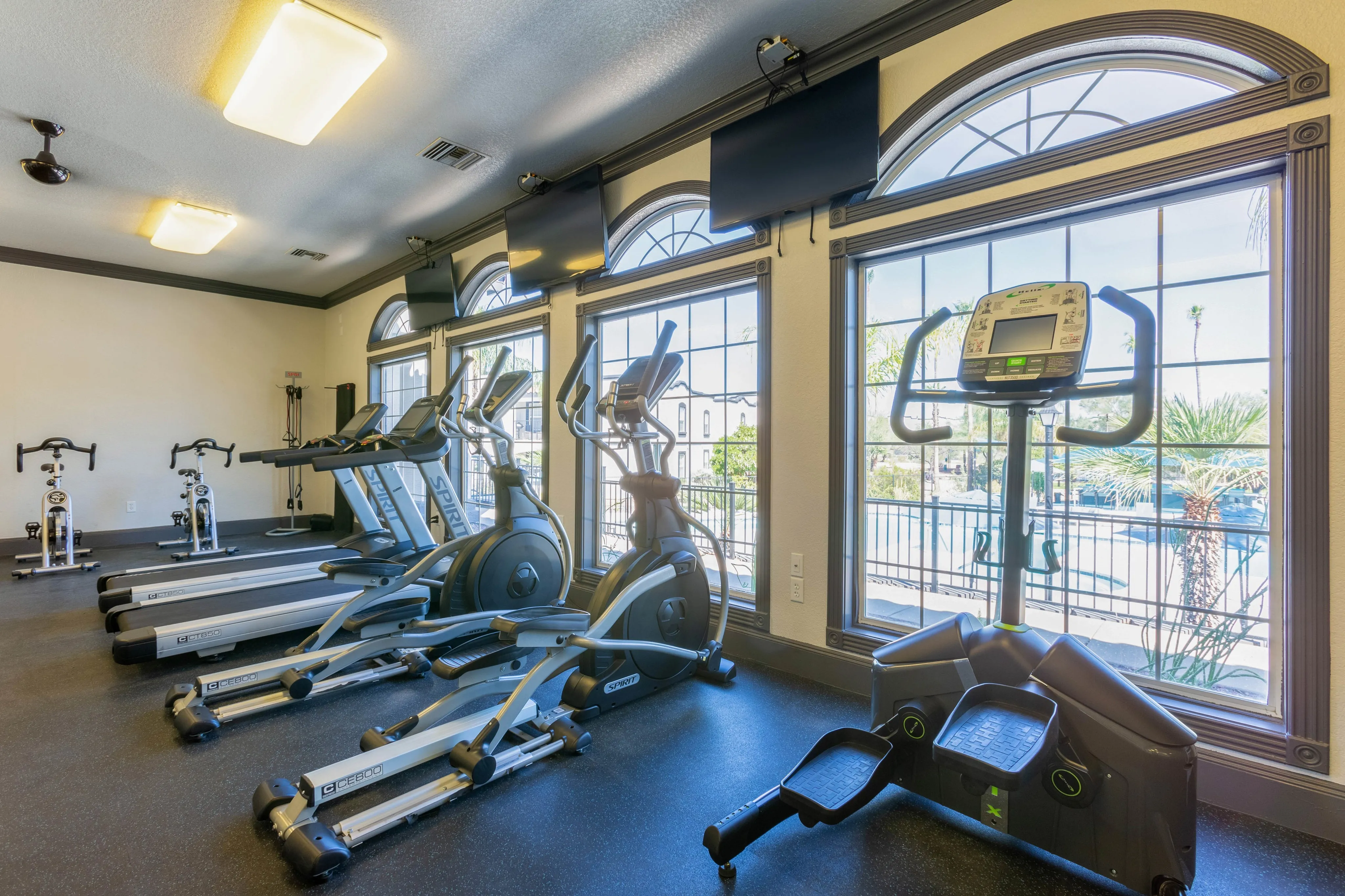 Resident fitness center with cardio equipment and large arched windows, offering views of the community at Ascension at Ironwood in Tucson, AZ.