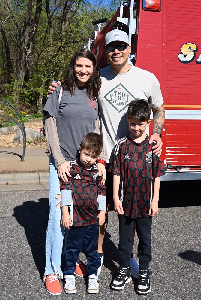 Saint Paul Firefighters Local 21 member with family posing in front of a fire truck during a community event.