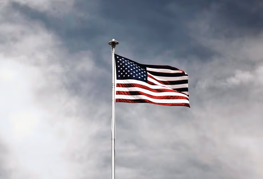 American flag flying on a tall pole against a cloudy sky.