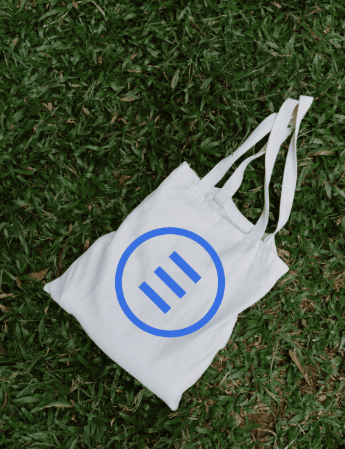 A tote back sitting in green grass with The Ethos Team logo on it.