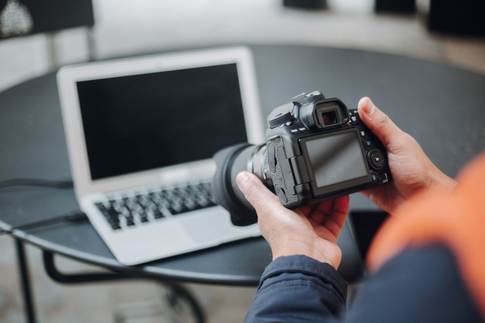 A person holding a mirrorless camera and a laptop for editing.