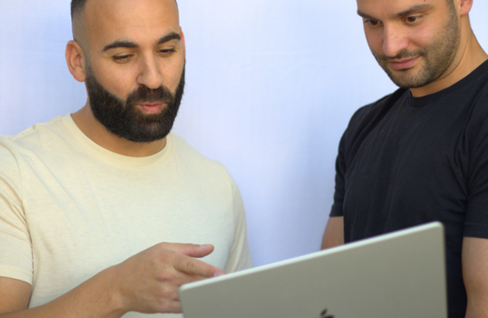 Two men looking at laptop together against light blue background