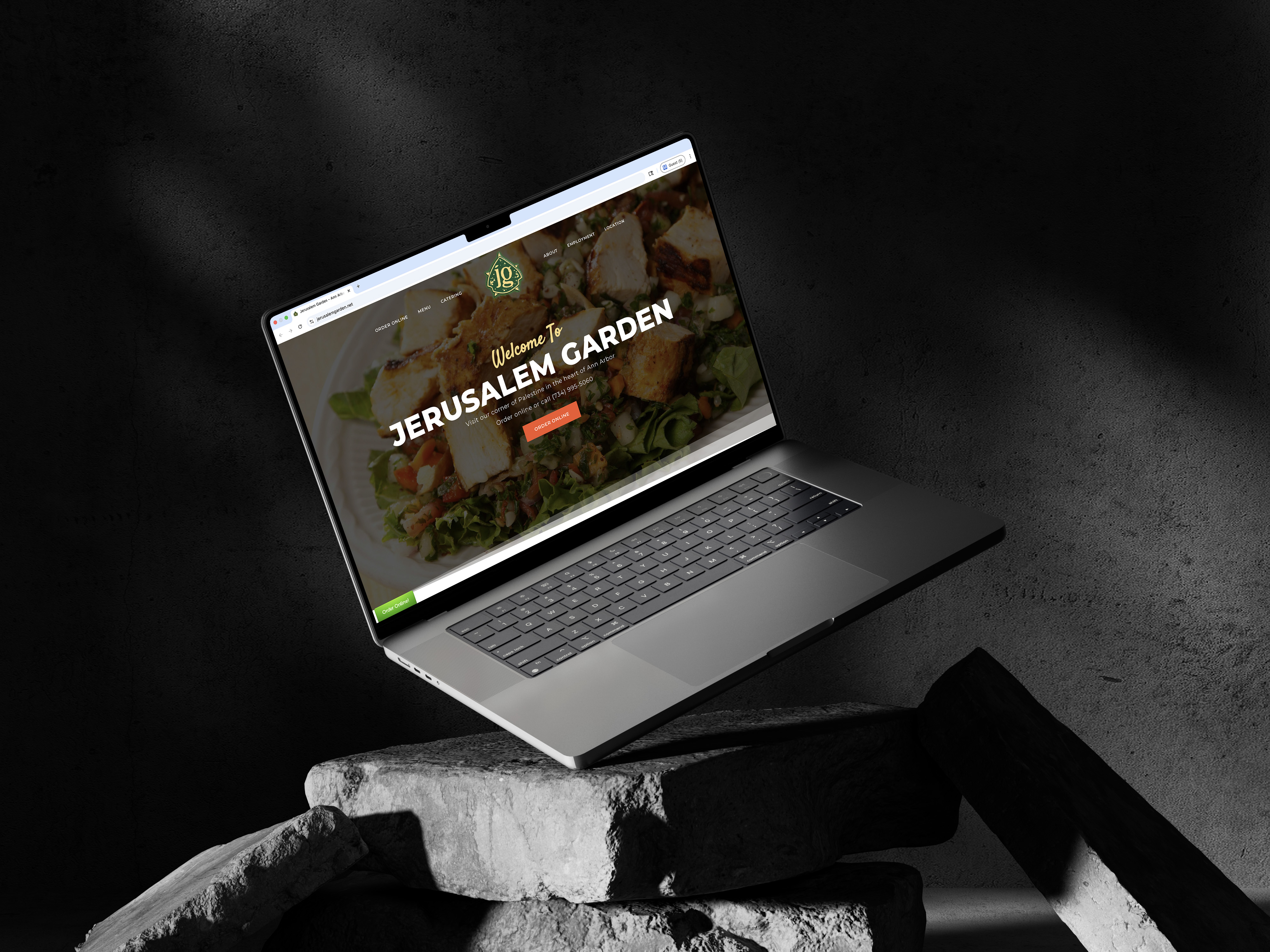 Laptop displaying Jerusalem Garden restaurant website on rocky surface