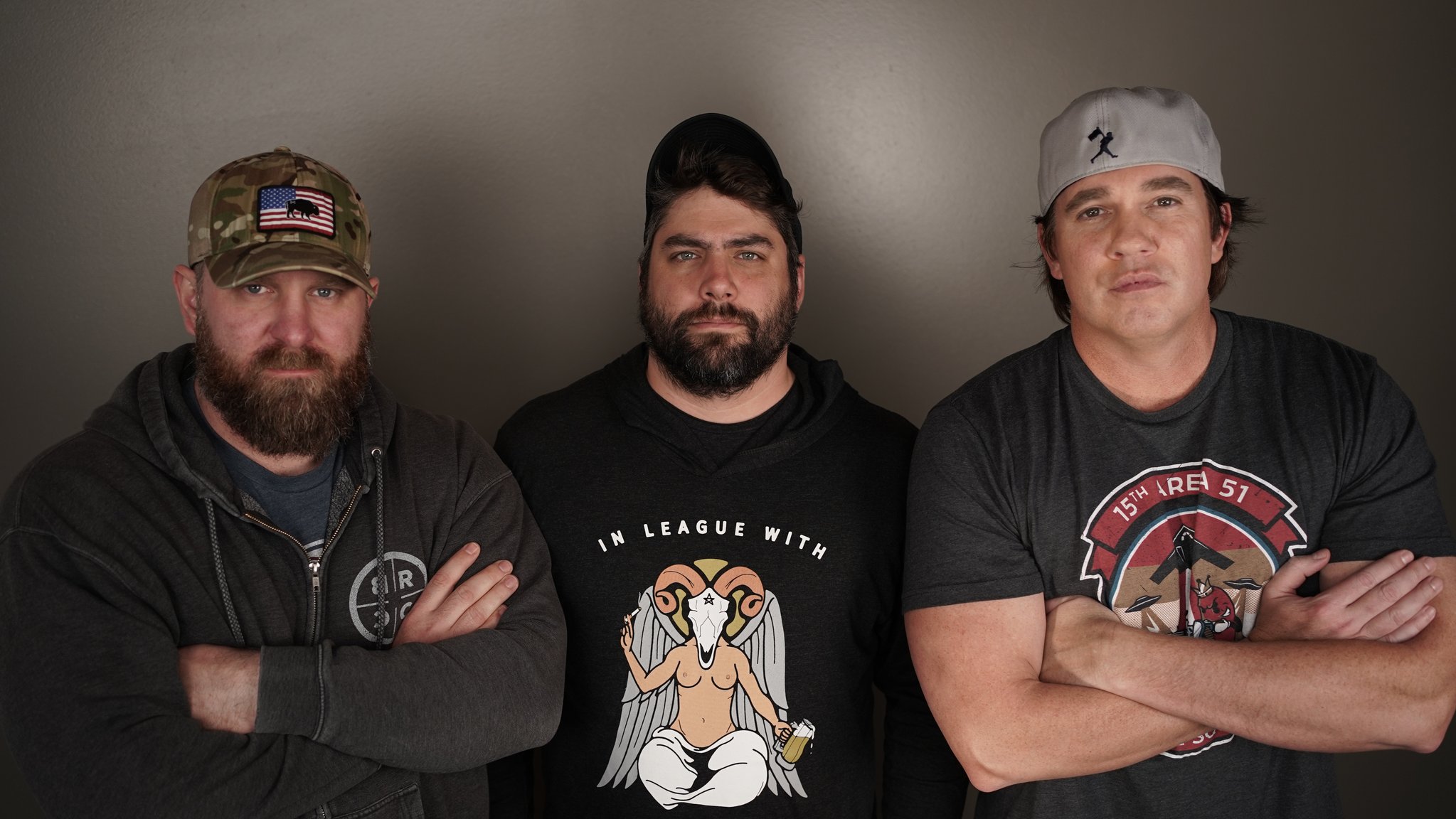 Three men in military-style shirts posing with crossed arms